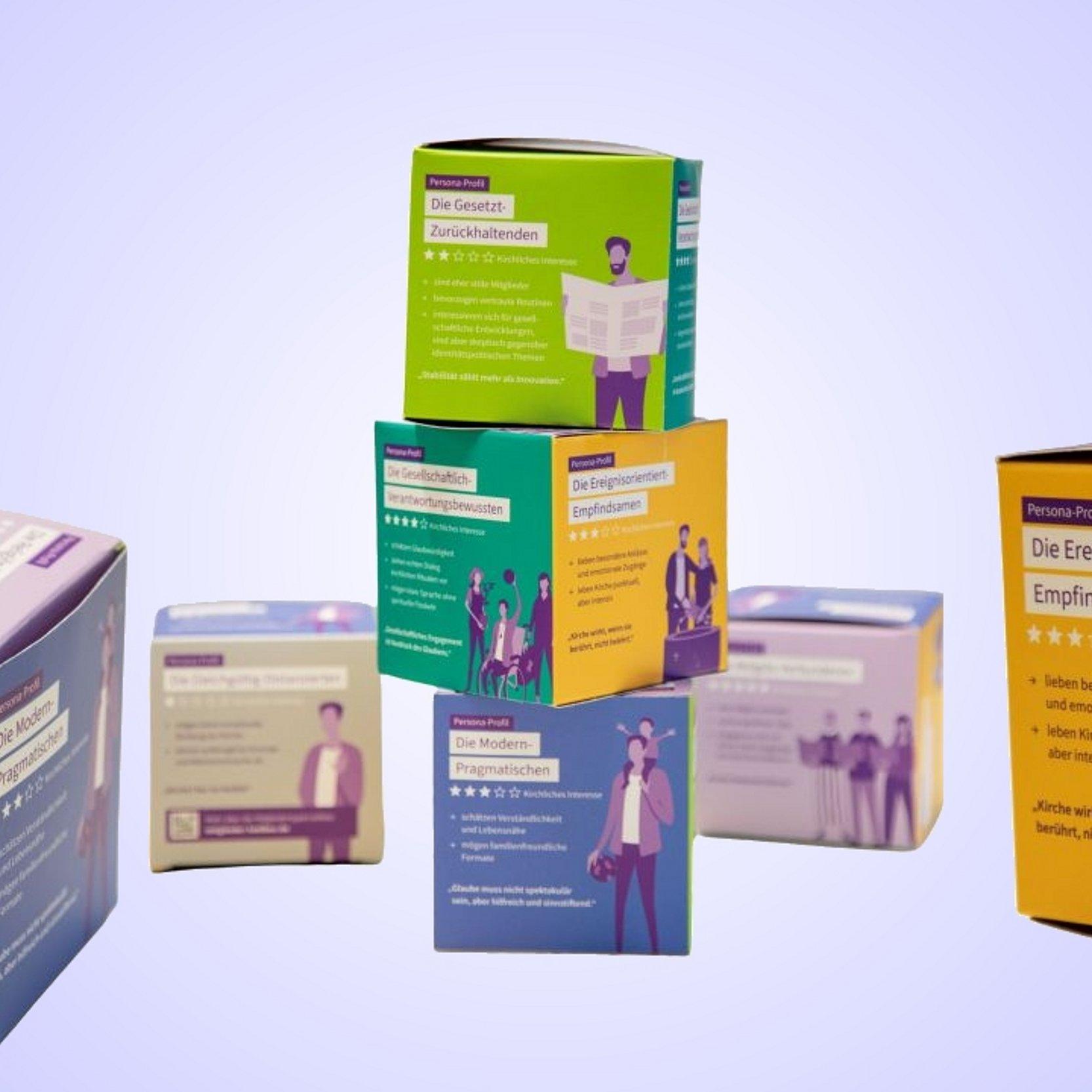 Toolbox Mitglieder im Blick Mehrere bunte, würfelförmige Boxen mit der Aufschrift „Persona-Profil“ sind gestapelt und angeordnet; sie zeigen verschiedene Charaktertypen mit stilisierten Illustrationen von Menschen und kurzen Beschreibungen auf Deutsch vor einem hellen Hintergrund.