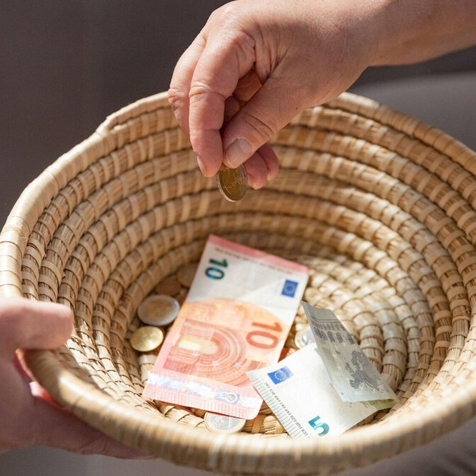 Kollektenkörbchen Ein geflochtenes Körbchen wird herumgereicht, um Geld einzusammeln. Ein paar Scheine und Münzen befinden sich bereits darin.