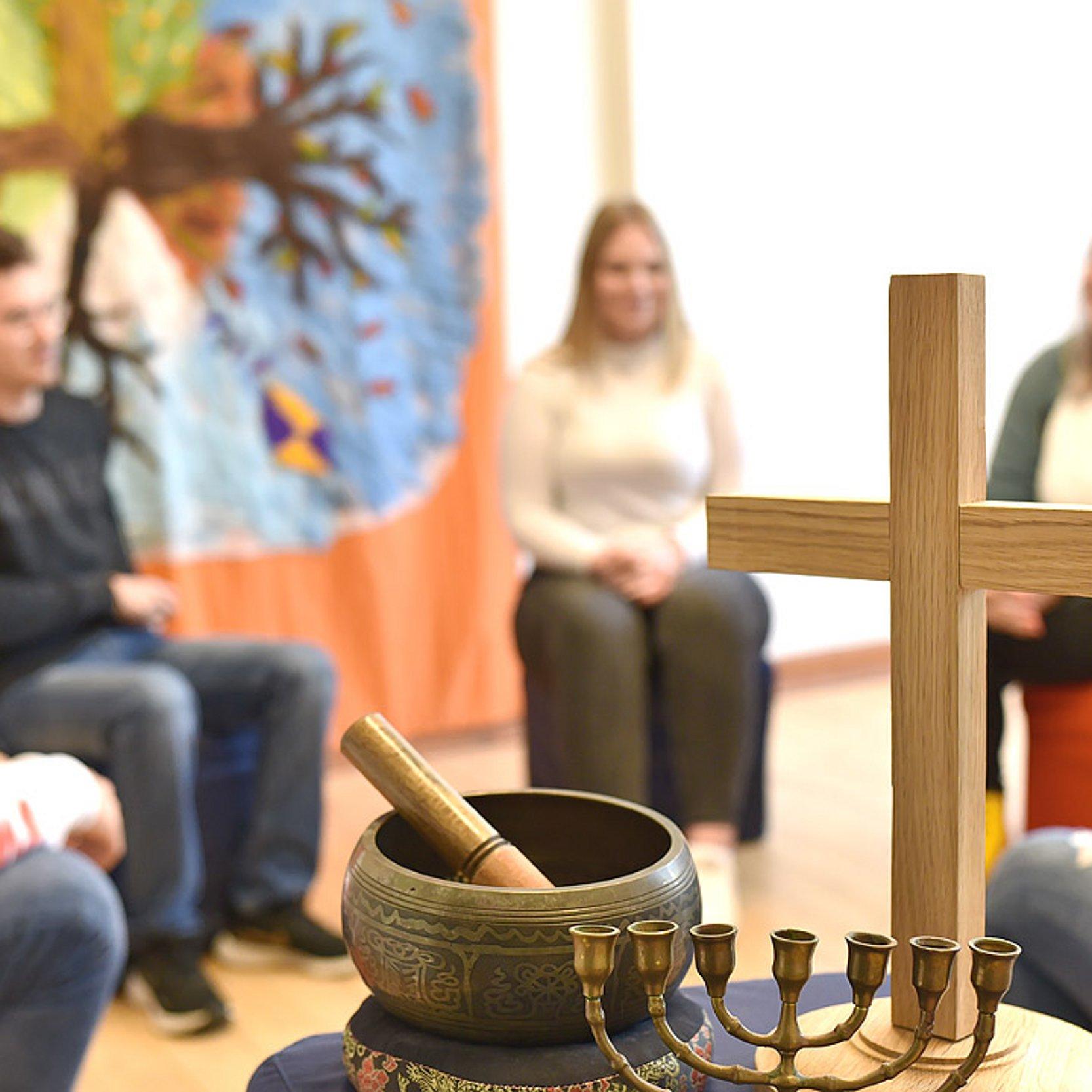 Meditation Oberstufenschüler sitzen im Kreis, davor sind ein christliches Kreuz, eine Klangschale und ein siebenarmiger Leuchter