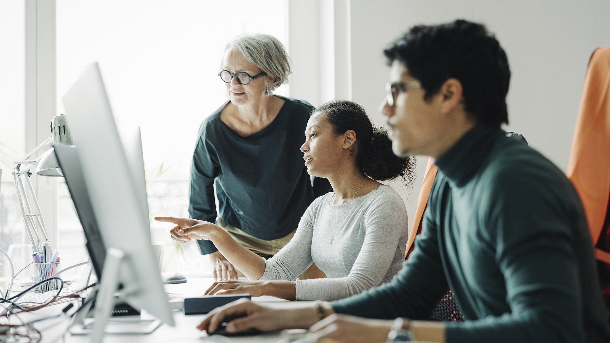 Zwei Frauen und ein Mann schauen auf einen Bildschirm.