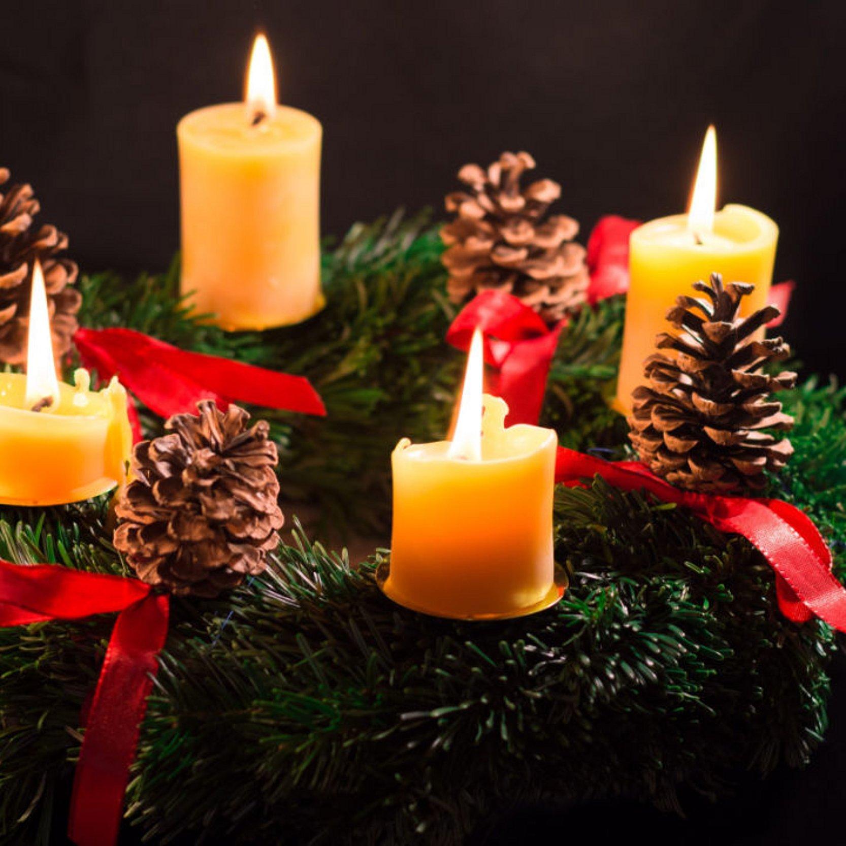 ein Adventkranz mit vier brennenden gelben Kerzen