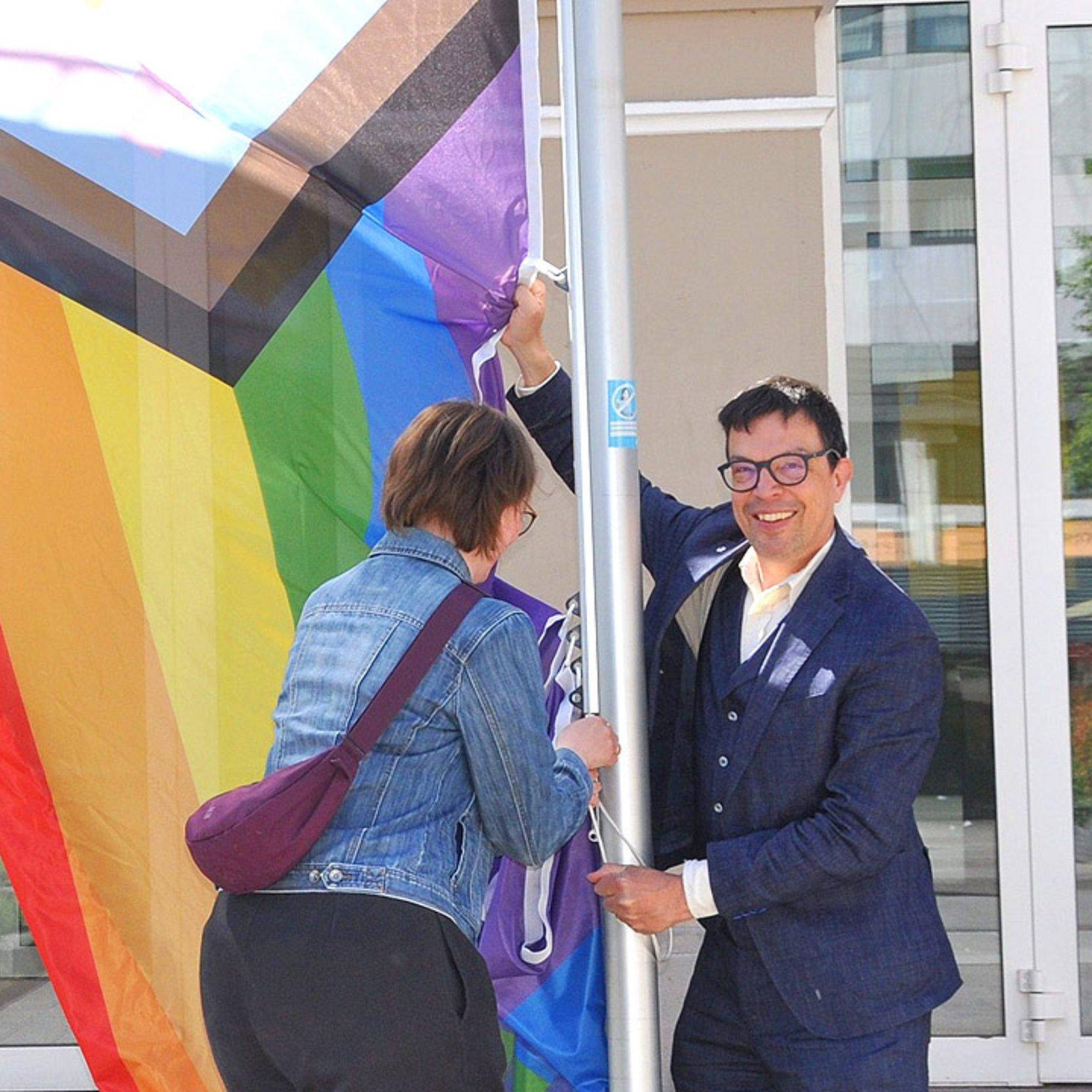 Flagge hissen Zwei Menschen ziehe eine bunte Flagge an einem Mast hoch