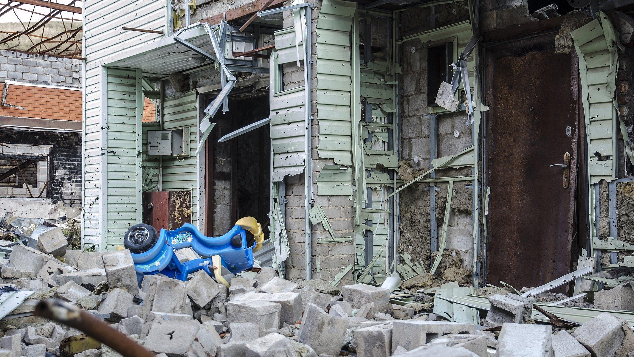 Krieg in der Ukraine. Ein zerstörtes Haus und davor ein Bobbycar für Kinder. Siedlung Shyrokyne, Donezk. September 2018.