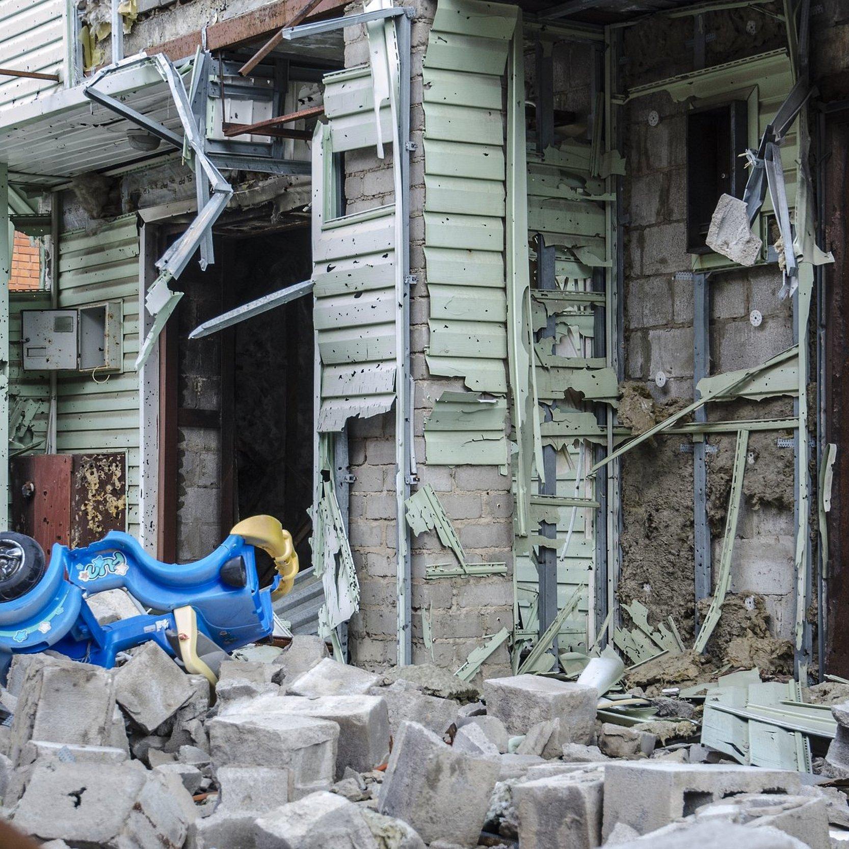 Krieg in der Ukraine. Ein zerstörtes Haus und davor ein Bobbycar für Kinder. Siedlung Shyrokyne, Donezk. September 2018.