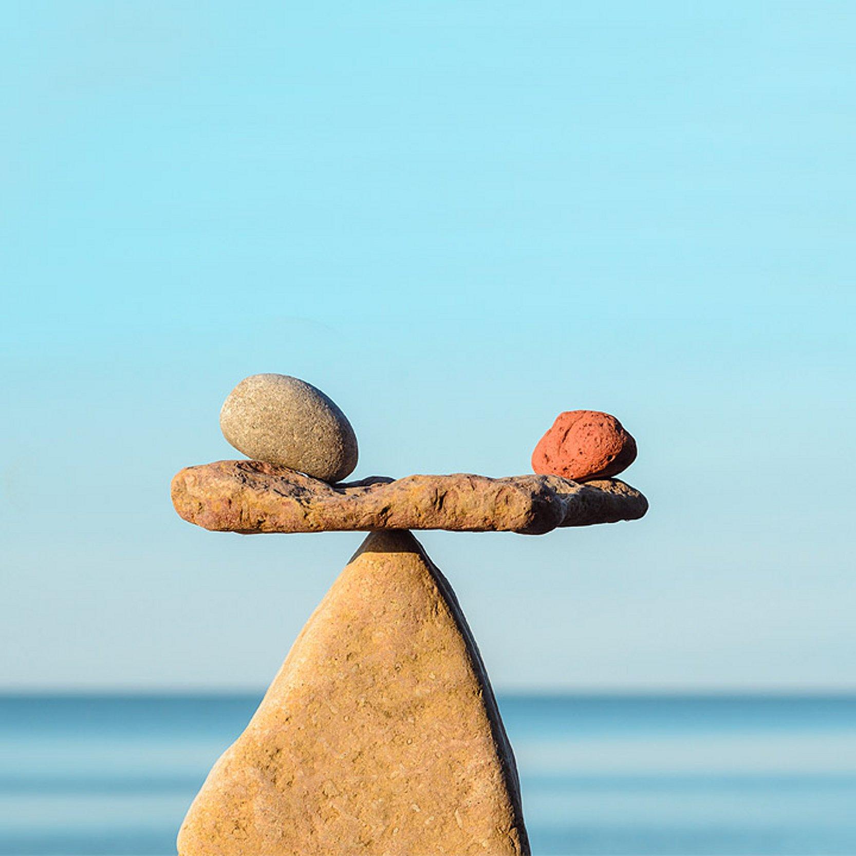 Klimafasten - Balance Steinmännchen am Meer in Form einer Waage, auf dem Querstein liegen links und rechts zwei kleiner Steine