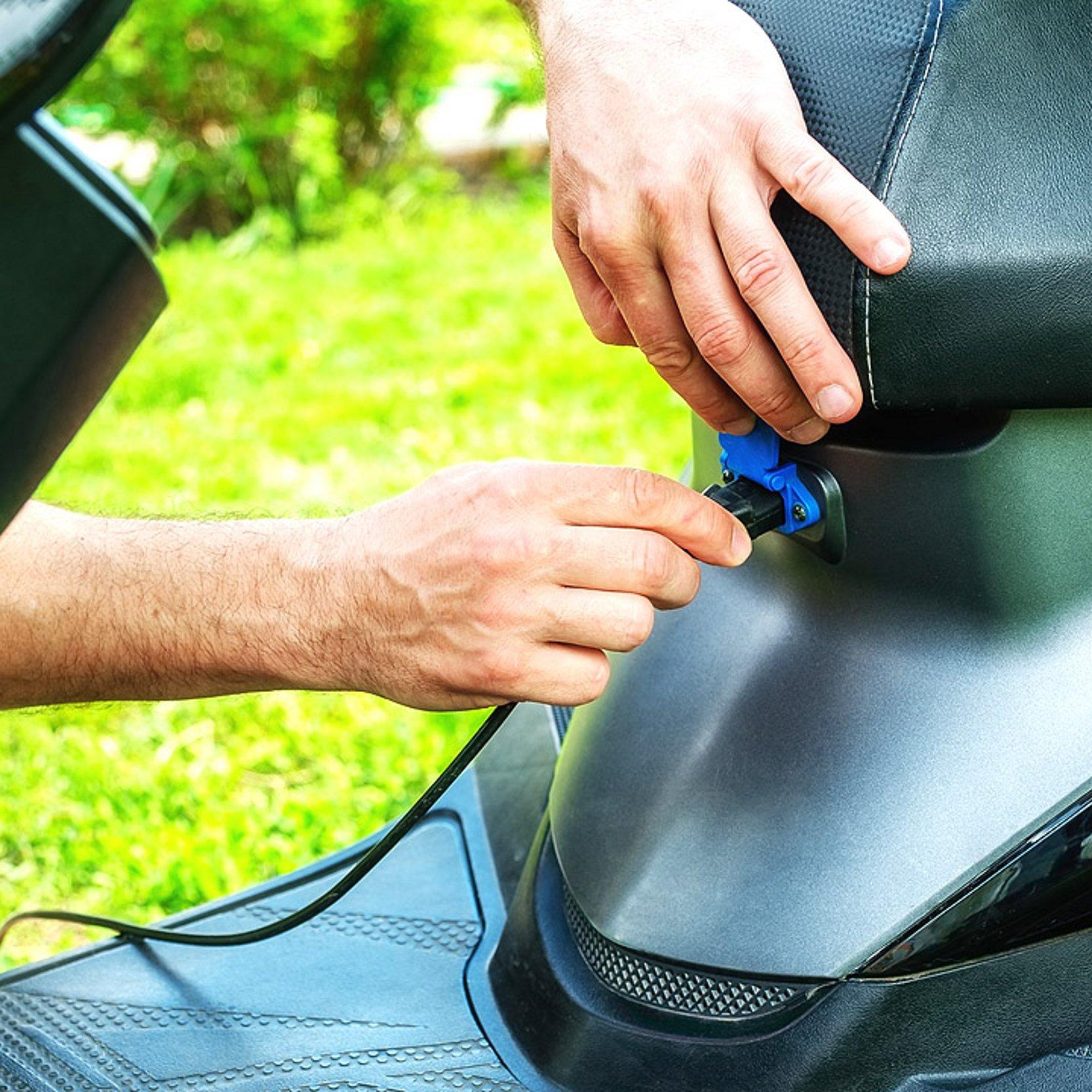 Elektroroller Eine männliche Hand steckt den Ladestecker in einen Motorradroller