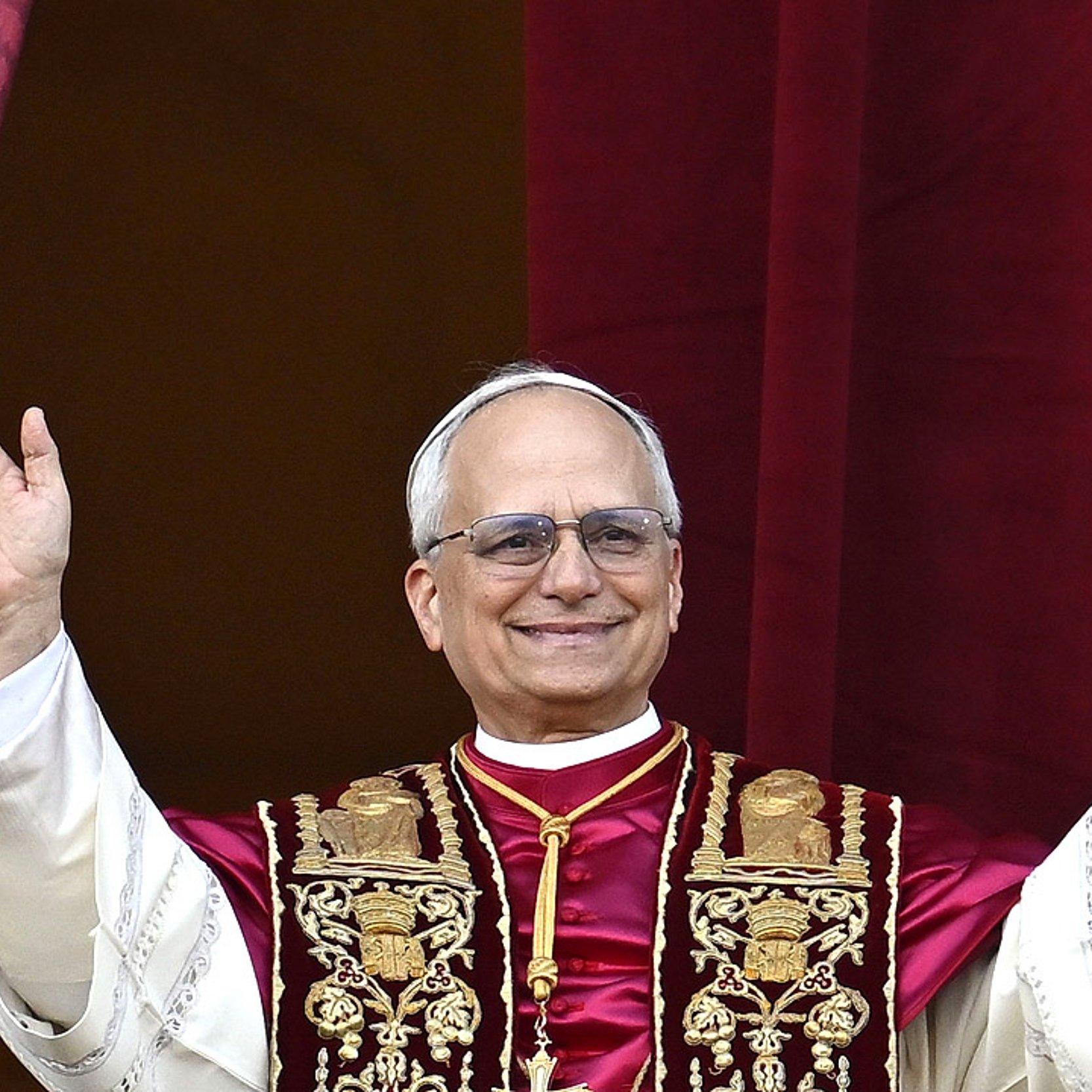 Papst Leo XIV. Papst Leo XIV. hebt die Hände und trägt ein weißes Gewand, darüber ein kürzeres bordeauxfarbene Seidencape und eine schwarz-goldene Stola um den Hals