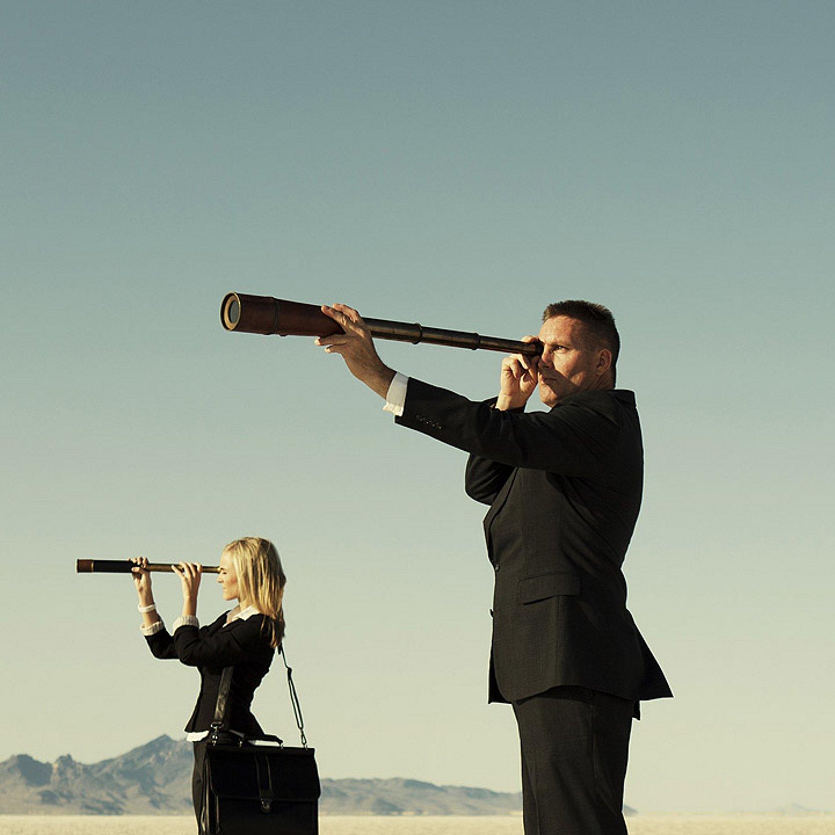 Projekt MaBiG Eine Frau und ein Mann in Business-Outfit mit Teleskop in einer Wüste