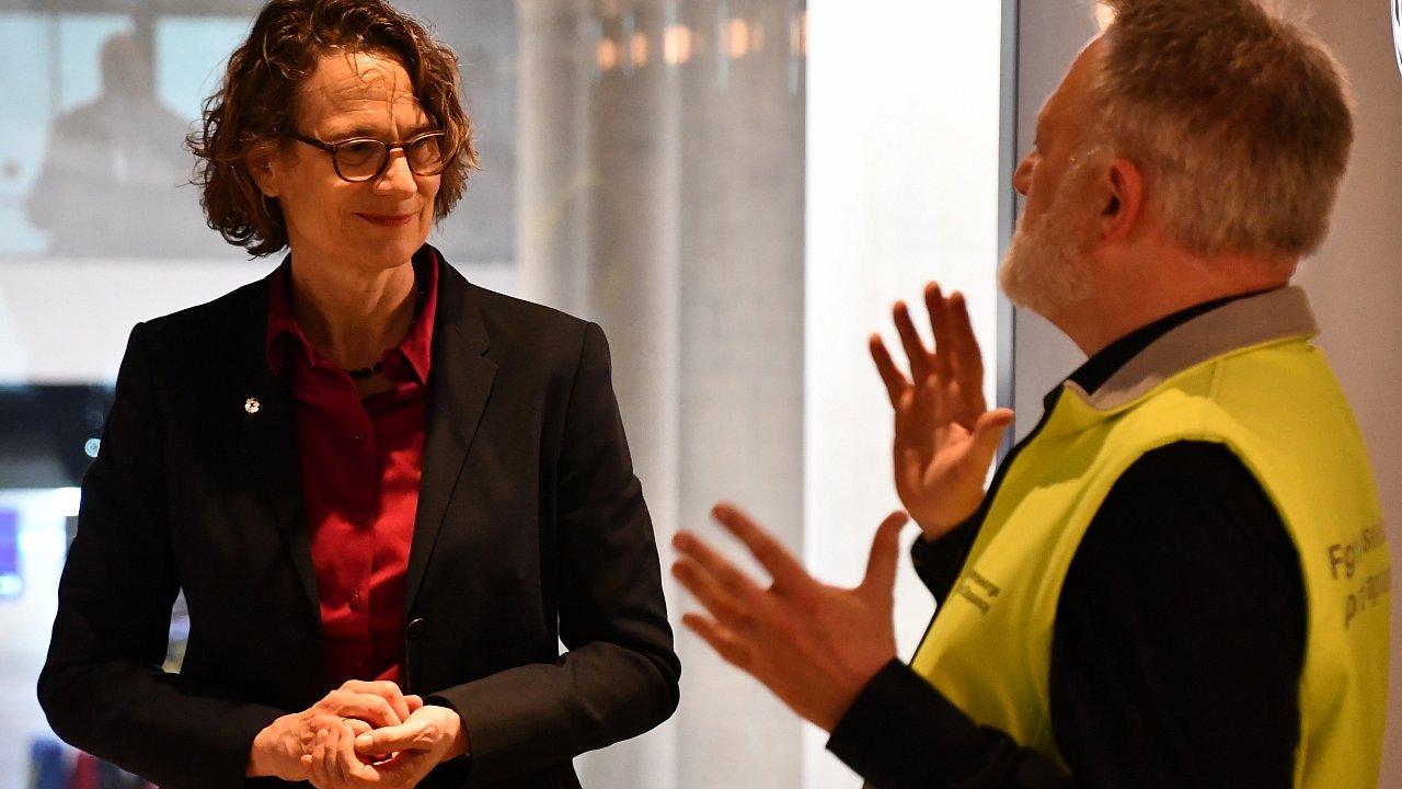 Tietz Flughafen Seelsorge Kirchenpräsidentin im dunklen Blazer und roter Bluse hört aufmerksam einem Seelsorger in einer gelben Sicherheitsweste zu, der mit erhobenen Händen gestikulierend spricht