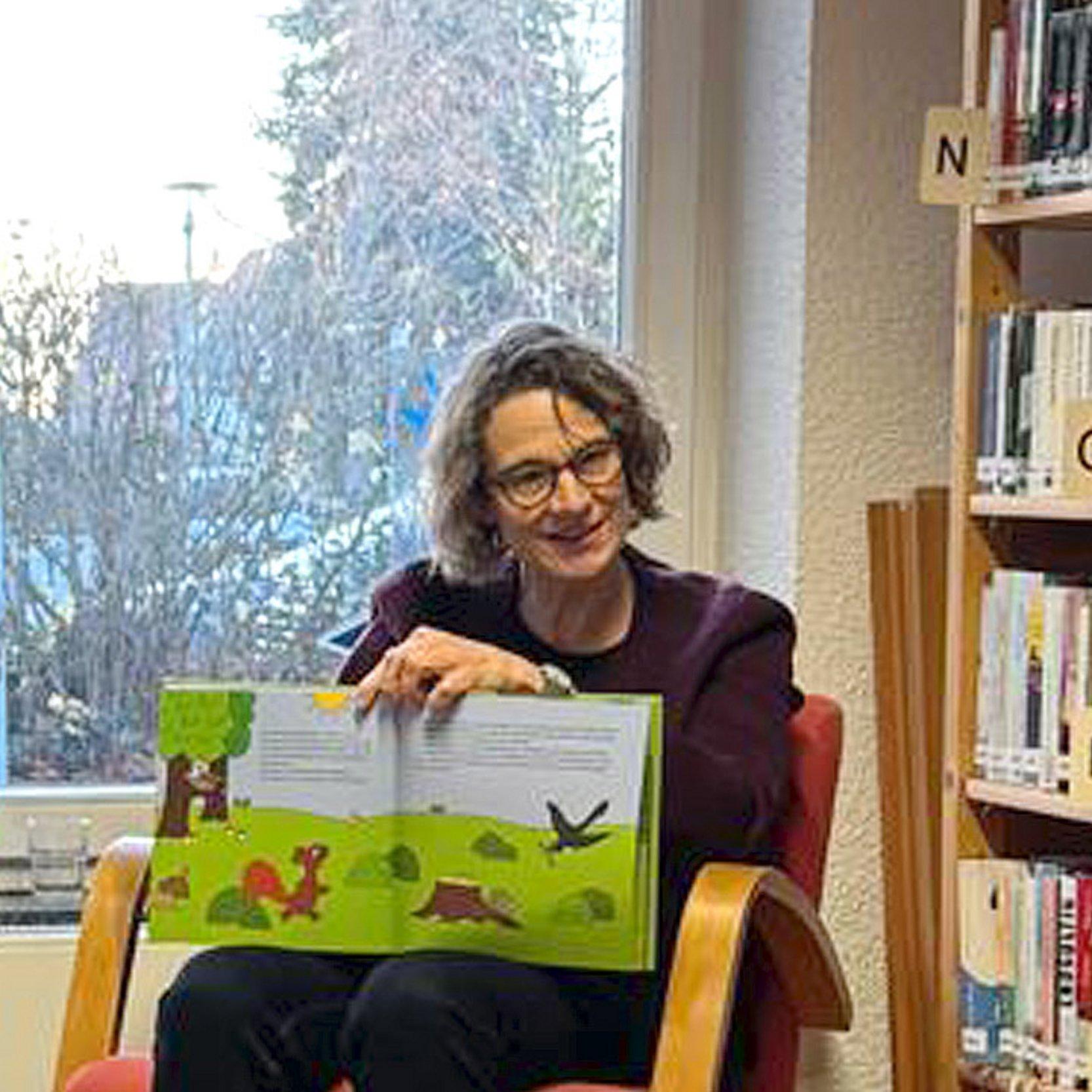 Vorlesetag Die Kirchenpräsidentin sitzt mit einem aufgeschlagenen Kinderbuch auf einem Stuhl