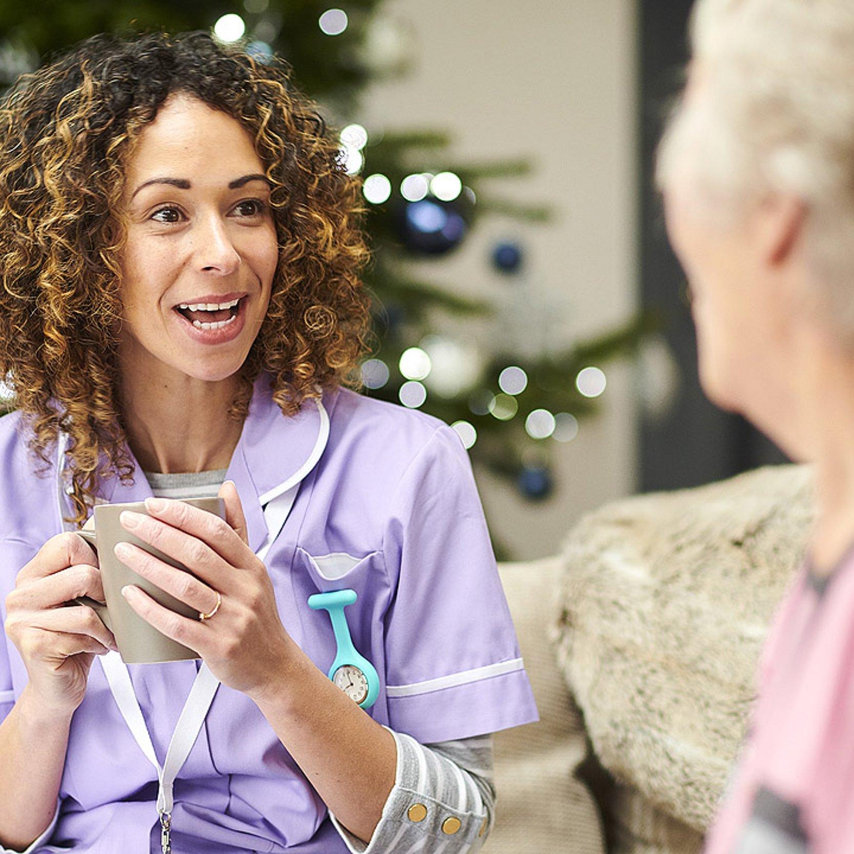 Weihnachten im Altenheim Pflegerin unterhält sich mit Seniorin, dahinter steht ein Weihnachtsbaum