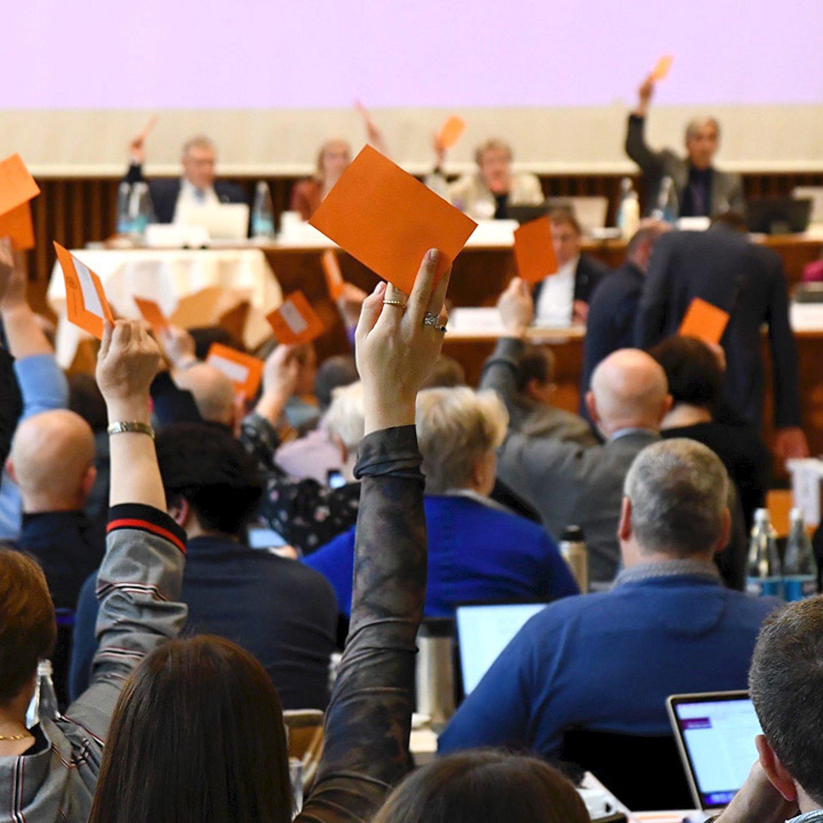 Synodenbeschluss Synodale heben einen orangenen Zettel hoch