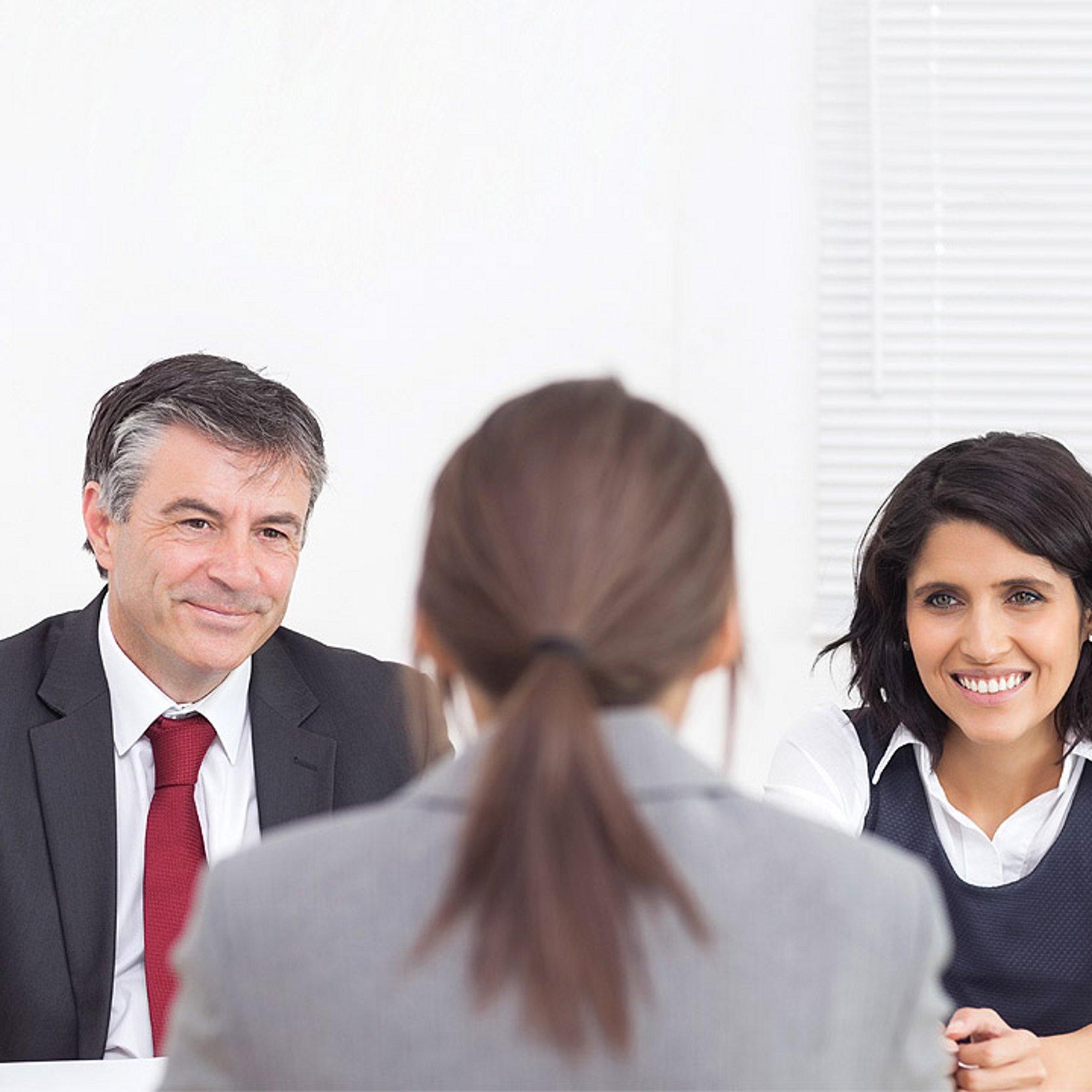 Bewerbungsgespräch Eine Bewerberin sitzt vor zwei Menschen, die das Bewerbungsgespräch führen