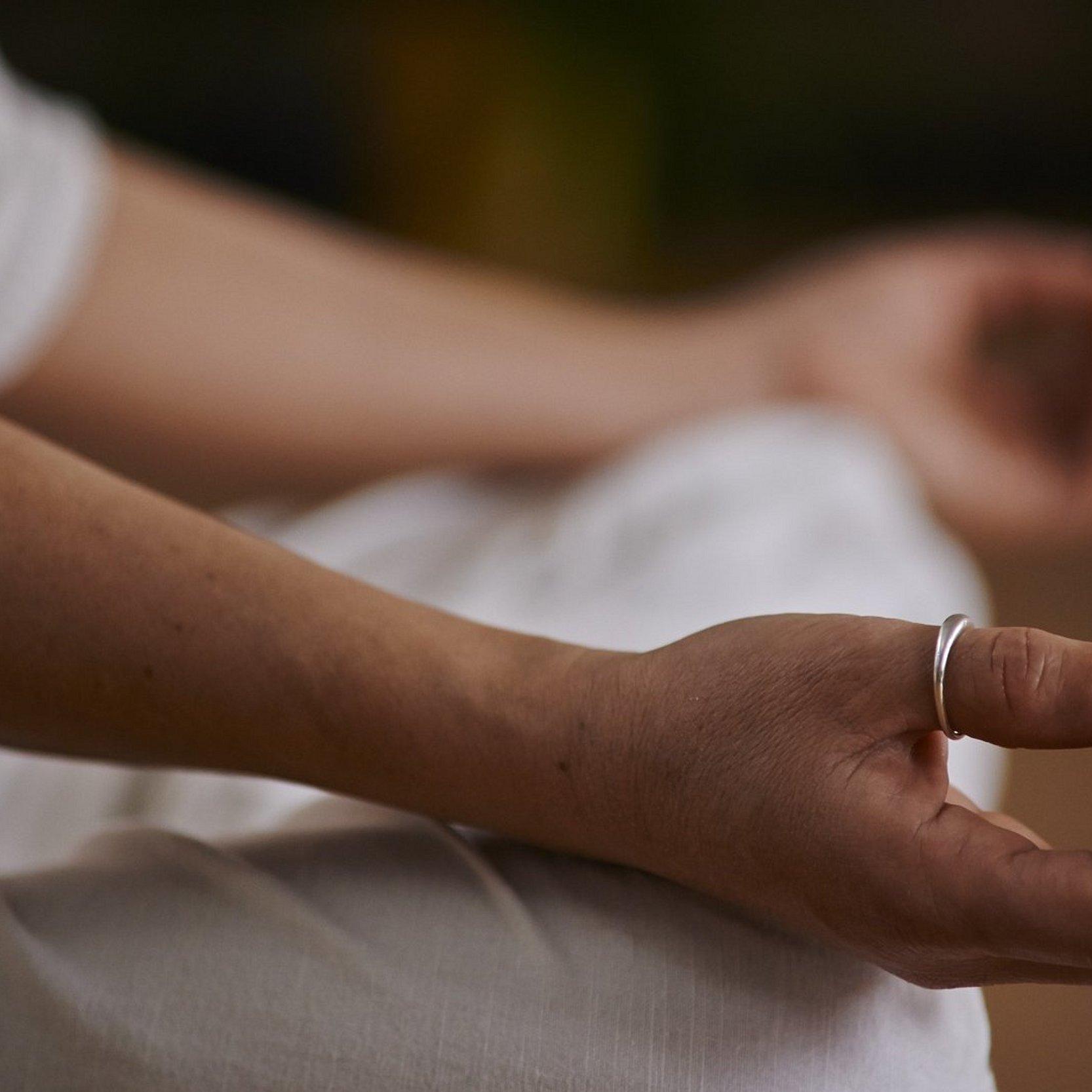 Bei einer Yoga-Übung liegen die Hände einer Person, die weiße Kleider trägt, auf ihren Knien.