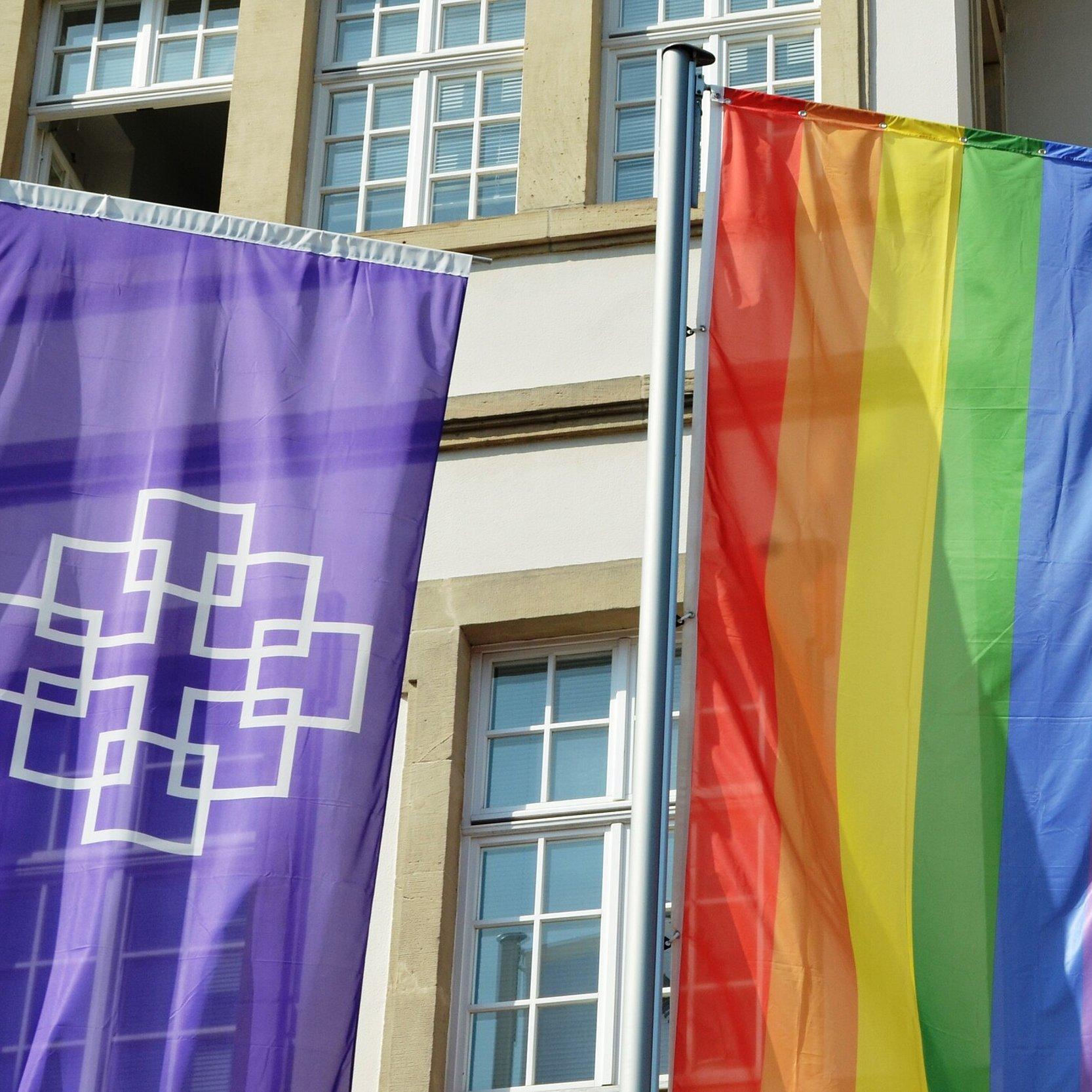 Fahnen vor der Kirchenverwaltung der EKHN Vor der Kirchenverwaltung der EKHN wurden neben der lila EKHN-Fahne mit Facettenkreuz anlässlich des CSD auch eine Regenbogenfahne gehisst.