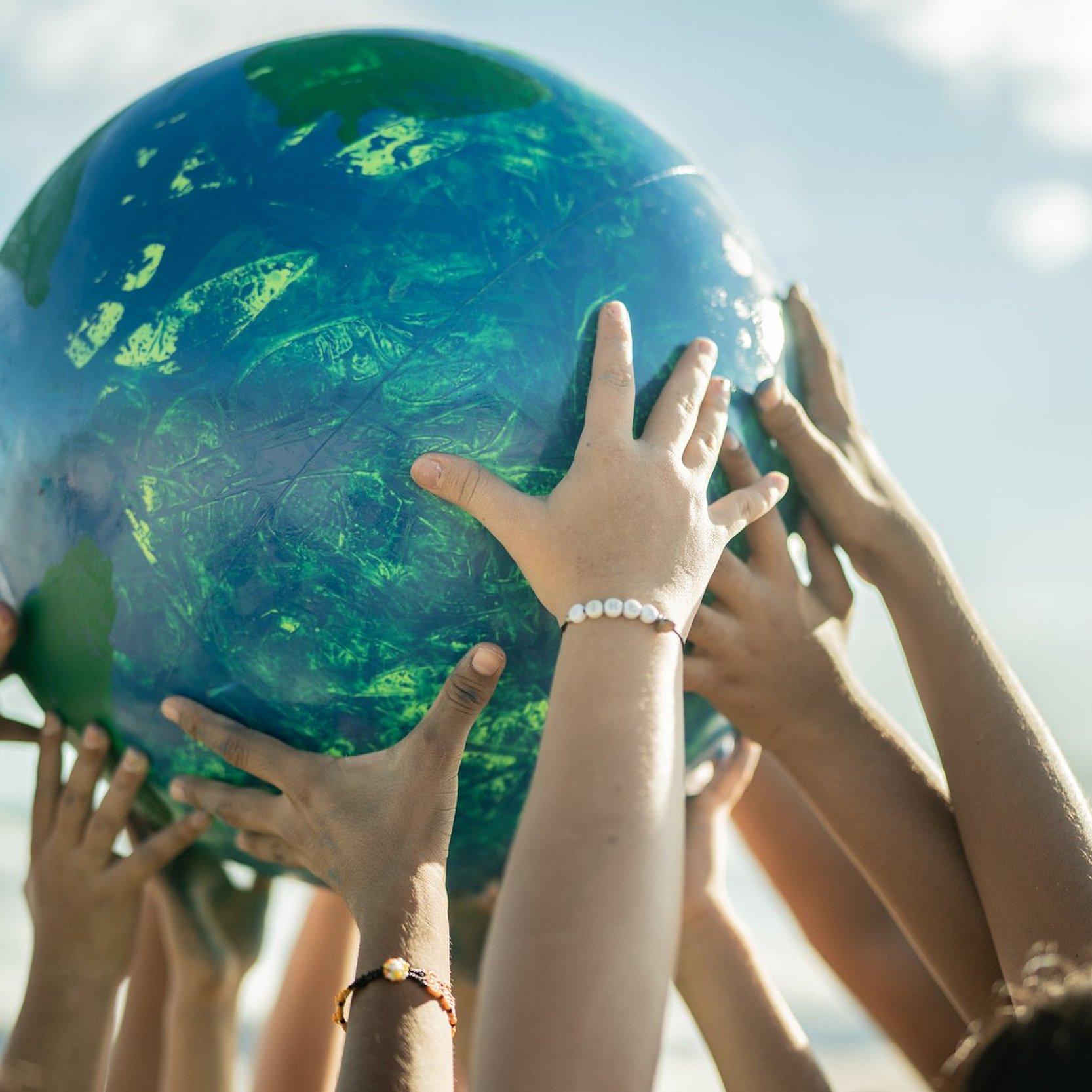 Gemeinsam anpacken, Klima schützen Viele Hände halten eine Weltkugel nach oben
