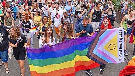 Jugendliche tragen eine große Flagge mit der Aufschrift: "Gott liebt queer."