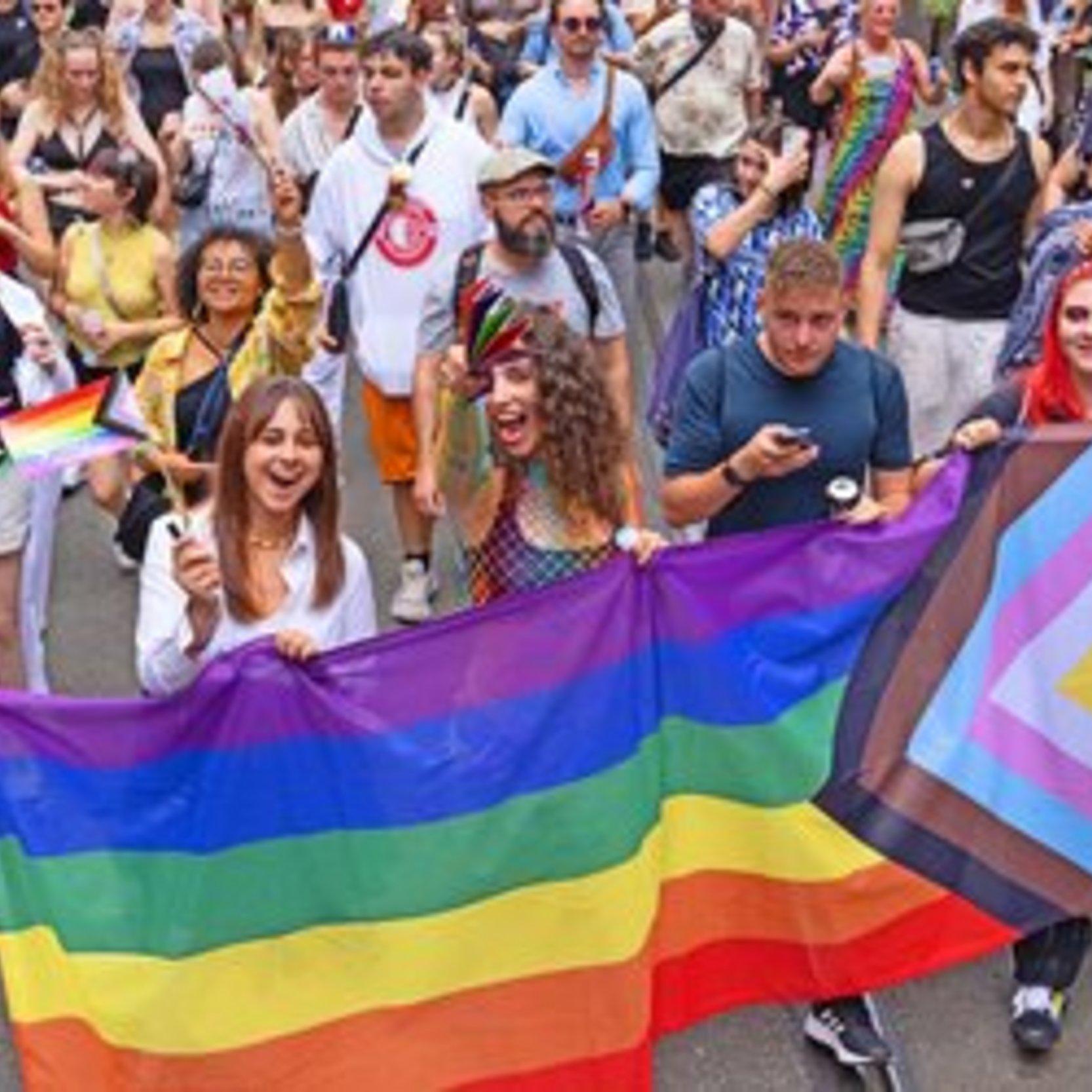 Jugendliche tragen eine große Flagge mit der Aufschrift: "Gott liebt queer."