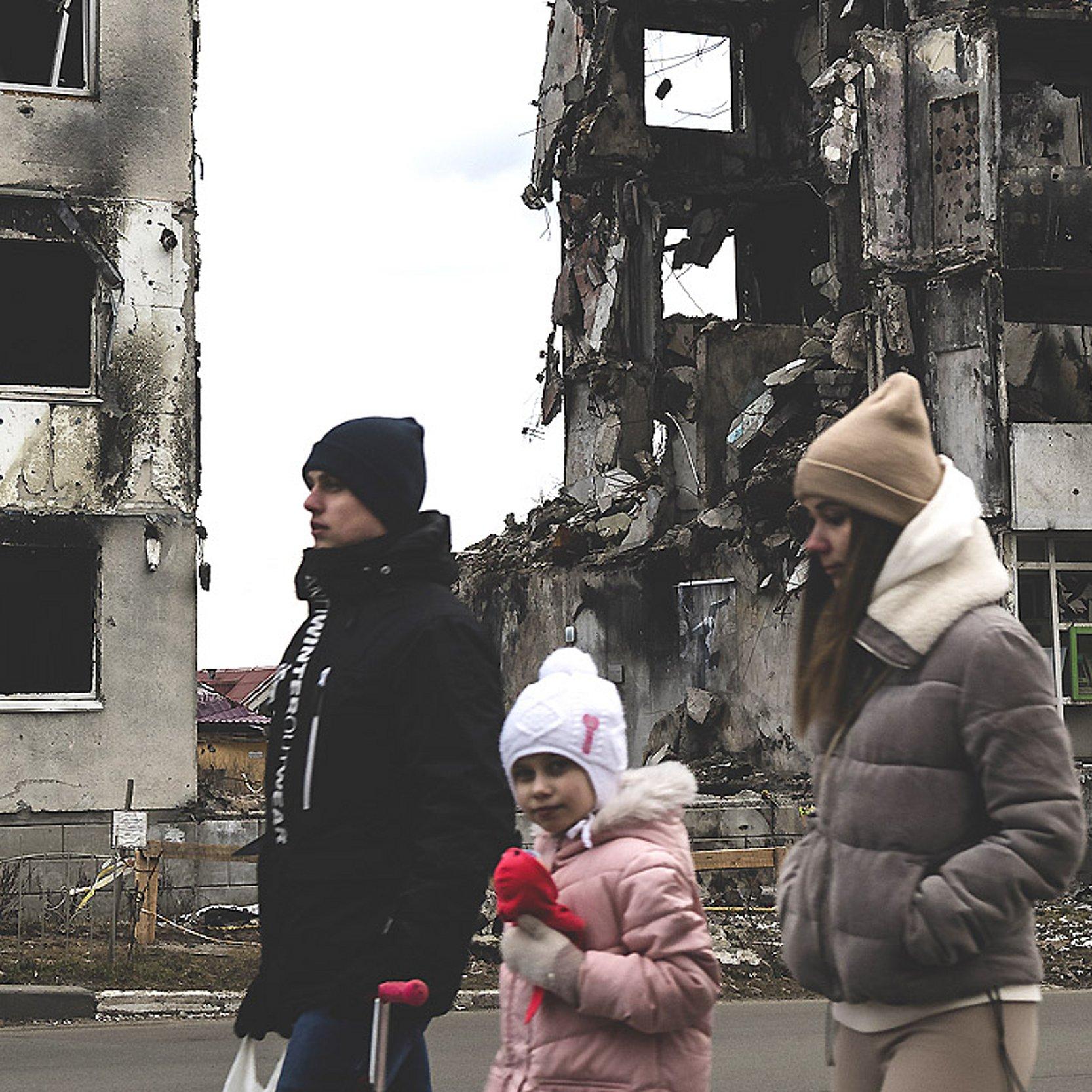 Ukraine, Krieg Familie läuft an Mietshaus-Ruinen vorbei