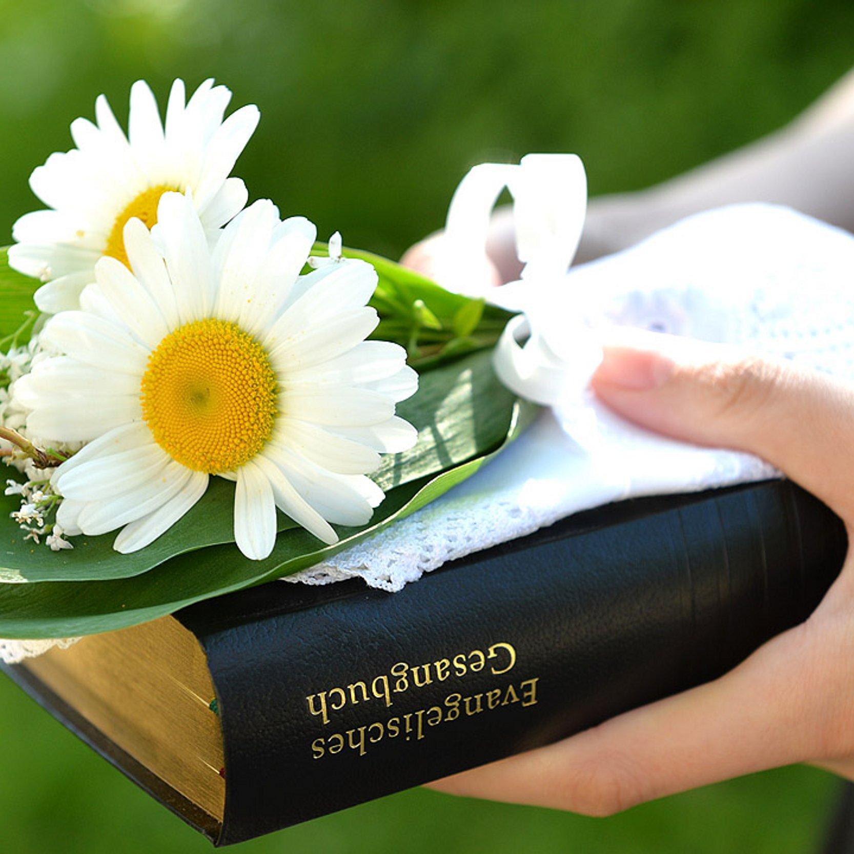 Konfirmation Hand, die einen Blumenstrauß und ein Gesangbuch hält