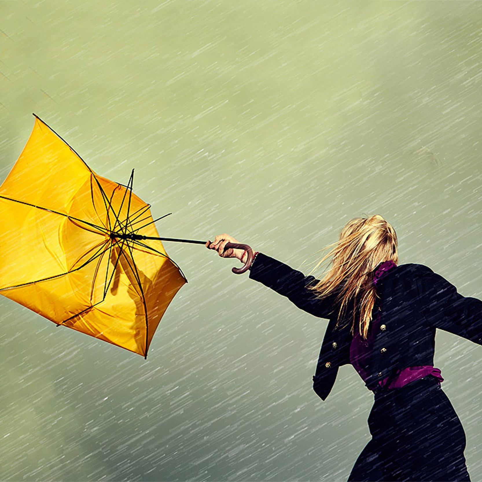 Sturm Der Wind bläst gegen einen gelben Regenschirm, den eine Frau noch gerade in der Hand hält und stülpt ihn um