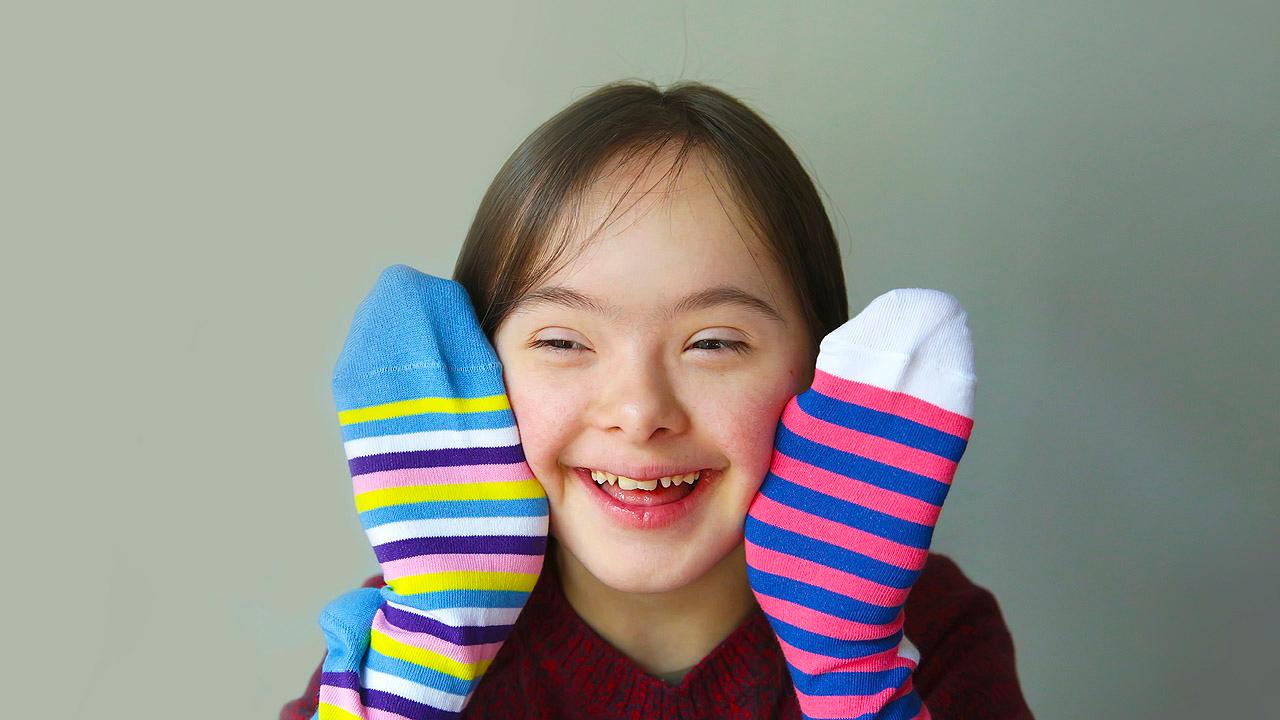 Mädchen mit Downsyndrom hält 2 bunte Socken hoch