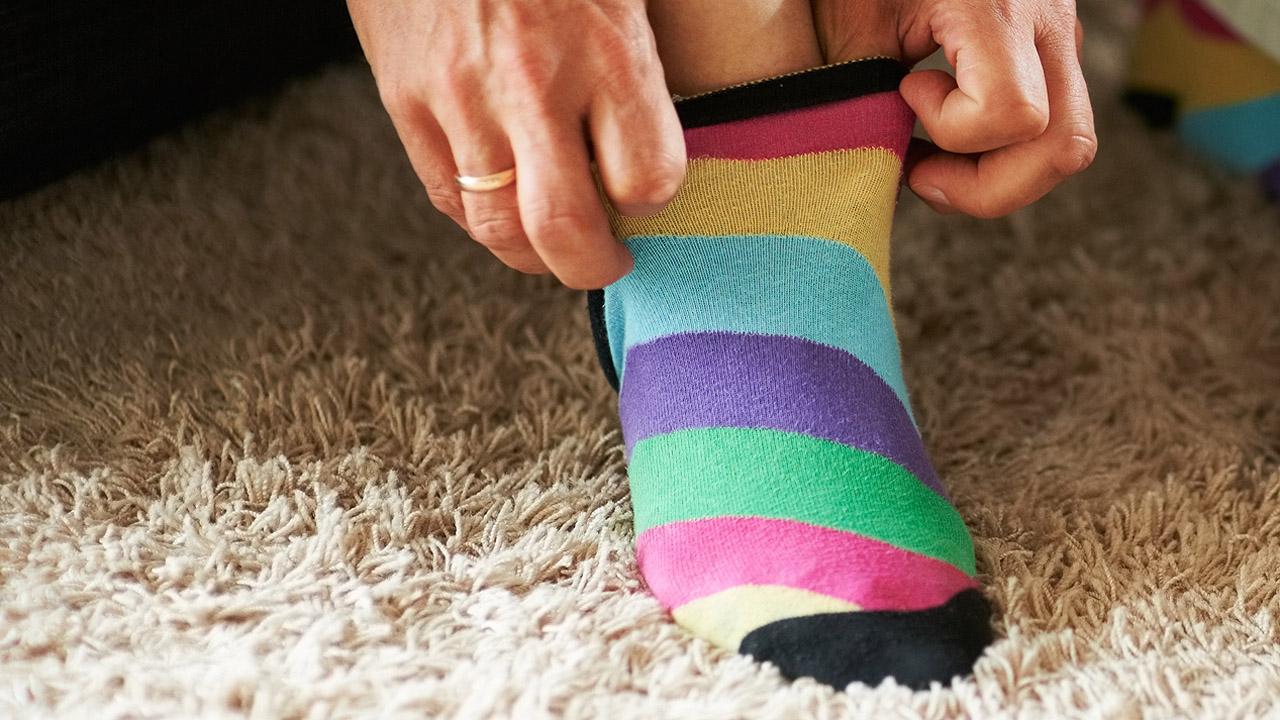 Bunte Socken Männliche Hände, die eine bunte Socke anziehen