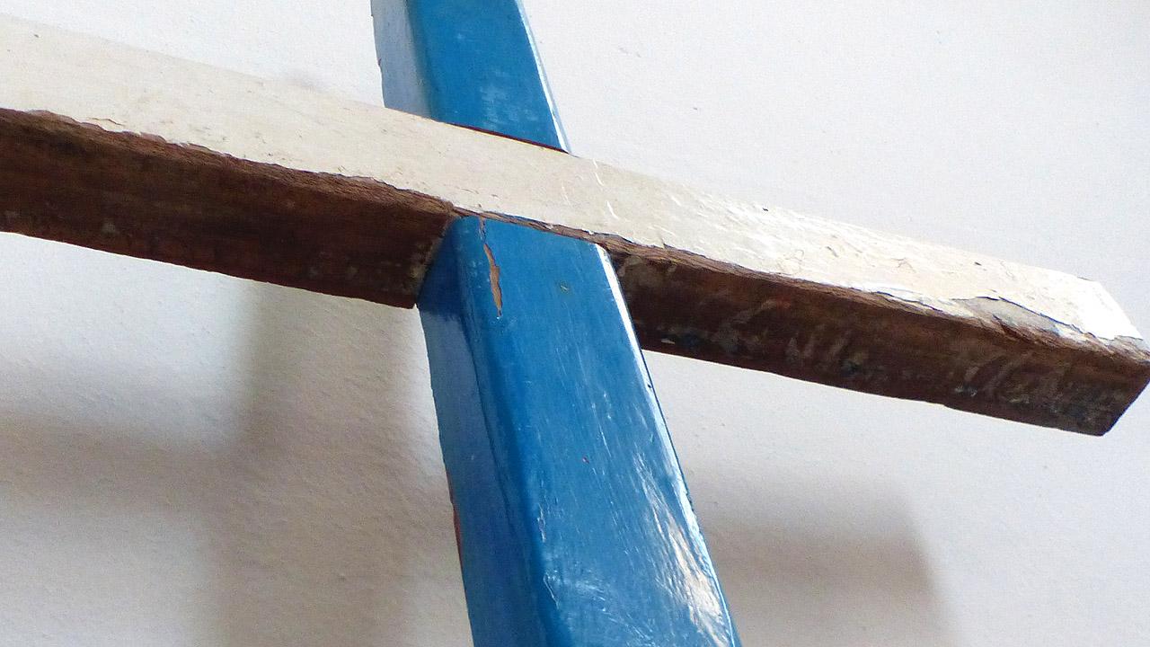 Ein Kreuz: Über einem senkrechten blauen Balken liegt ein brauner Holzbalken