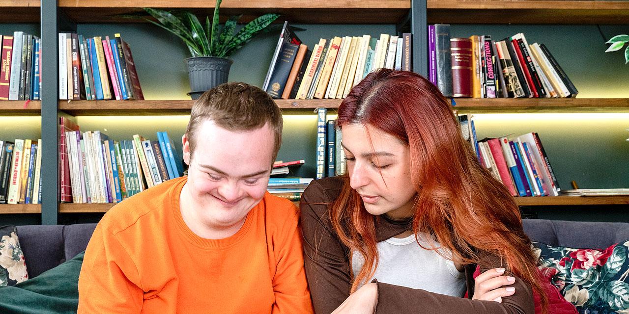 Eine Frau zeigt einem behinderten, jungen Mann den Umgang mit einem Laptop