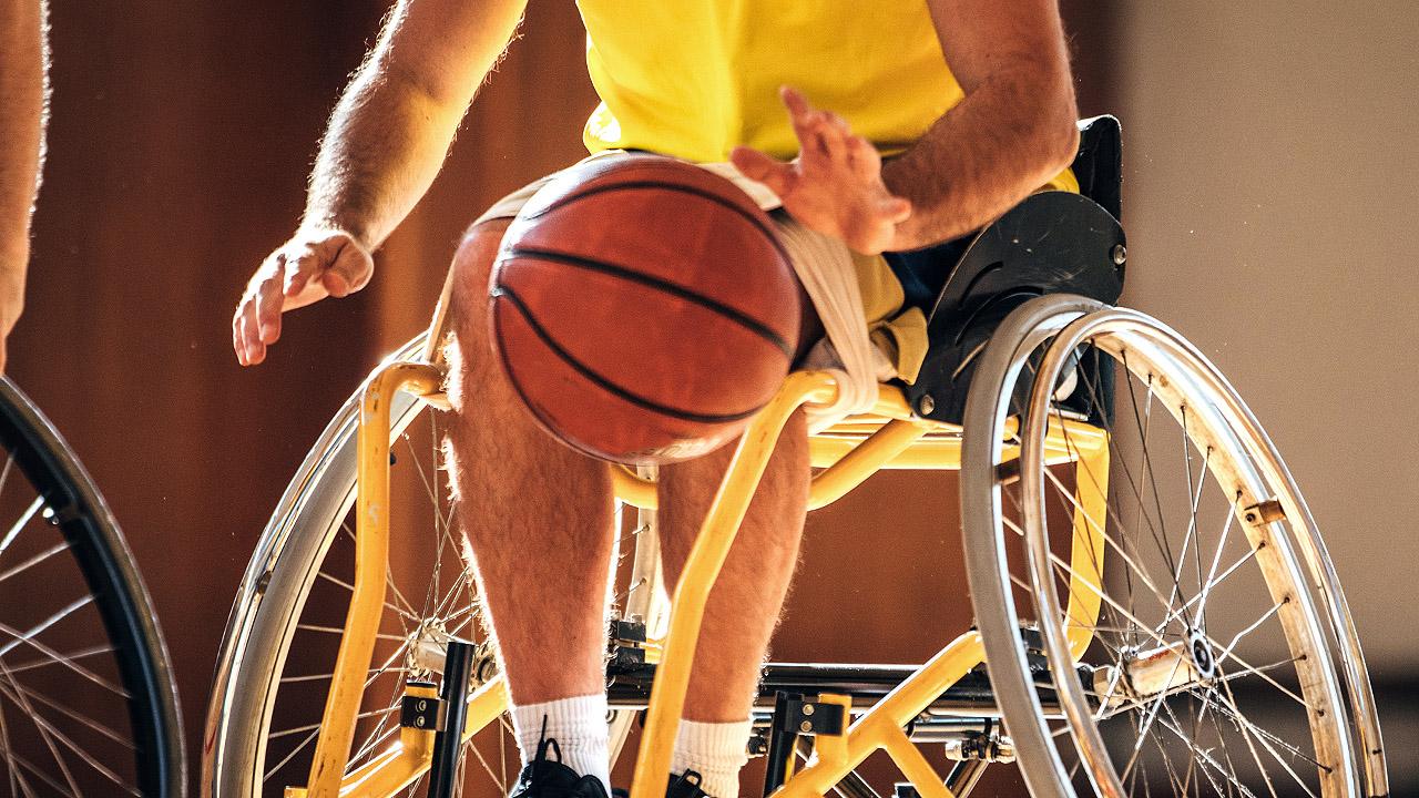 Ausschnitt eines Rollstuhlbasketballer in Aktion - ein Mensch sitzt im Rollstuhl, davor ein ein Basketball