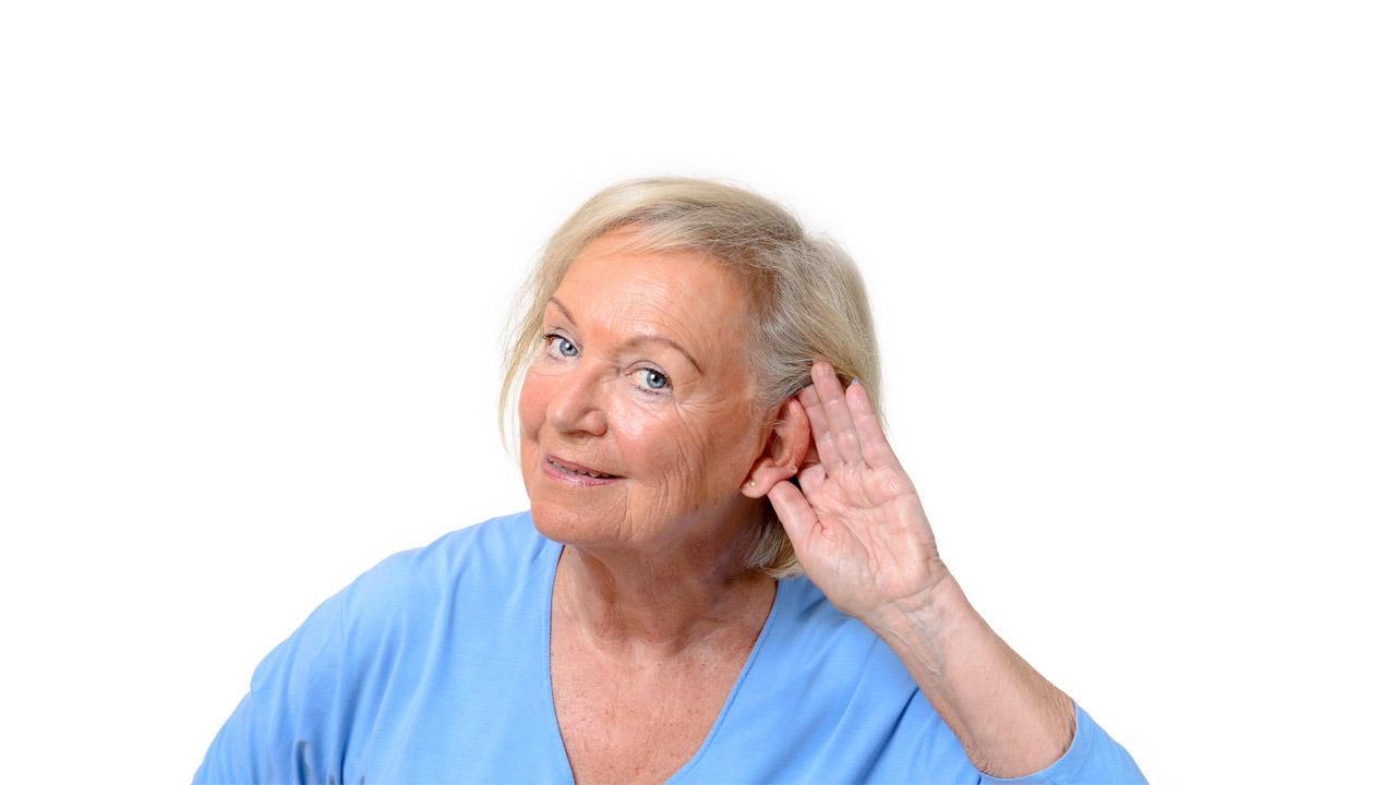Eine ältere Dame, die die Hand hinter ihre Ohrmuschel hält