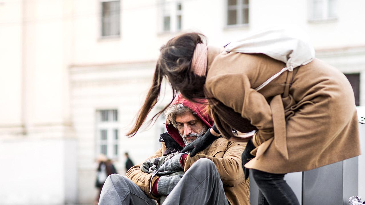 Passantin spendet einem obdachlosen Mann etwas