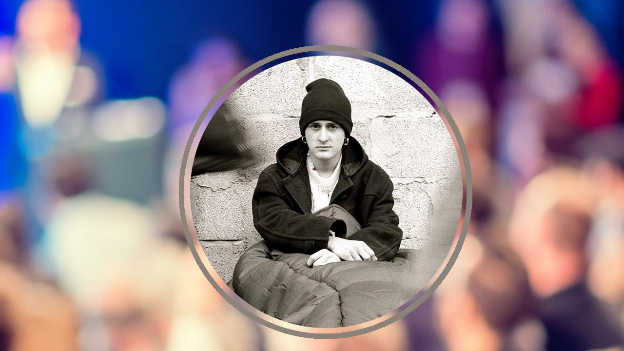 Obdachloser junger Mann vor einer unscharfen Menschenmenge