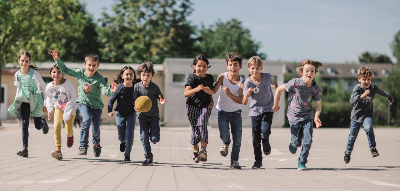 Eine Gruppe Kinder rennt gemeinsam über den Schulhof aus die Kamera zu.