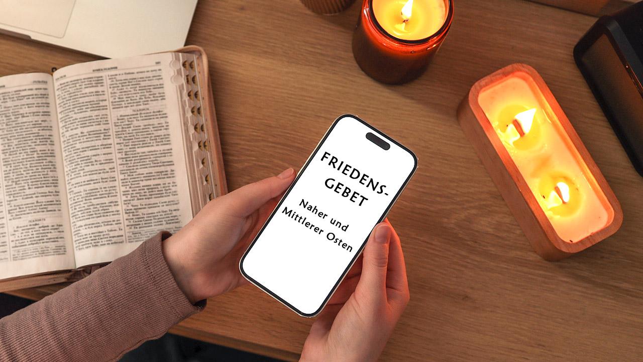 Kerzen, Laptop und Smartphone, auf dem "Friedensgebet - Naher und Mittlerer Osten " steht