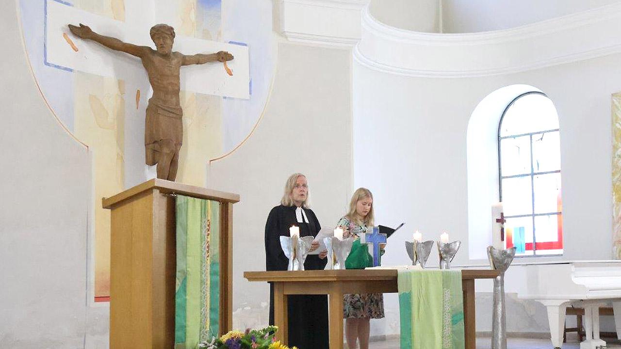 Gottesdienst Pfarrer und eine Frau hinter einem Altar vor einem großen, geschnitzen Jesus am Kreuz