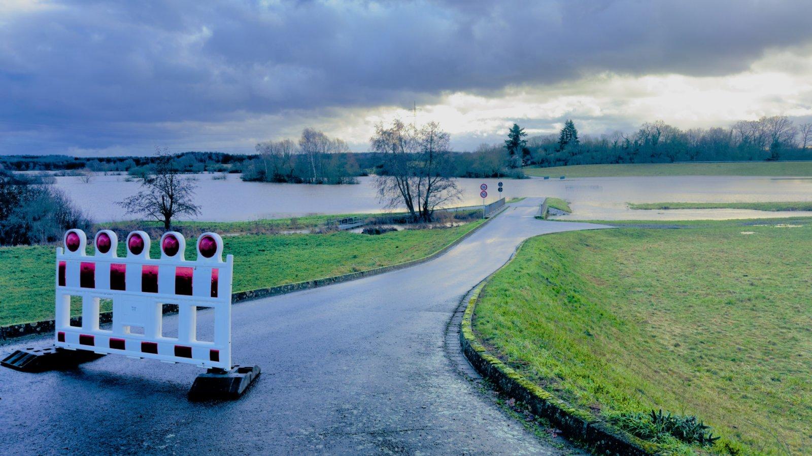 Überschwemmtes Flussgebiet mit abgesperrter Straße