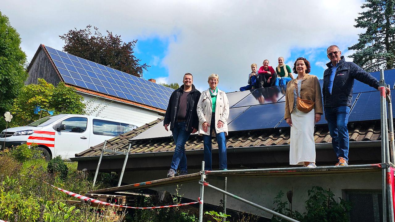Elektro-Bürgerbus Ein weißer Klein-Bus mit roten Streifen und eine Photovoltaikanlage auf einem Dach sowie eine Gruppe mit Menschen