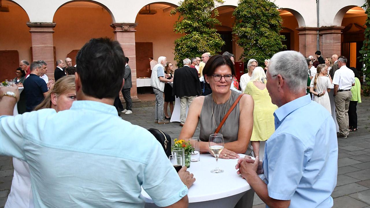 Sommerlicher Abend Menschen an Stehtischen in einem Innenhof sprechen miteinander