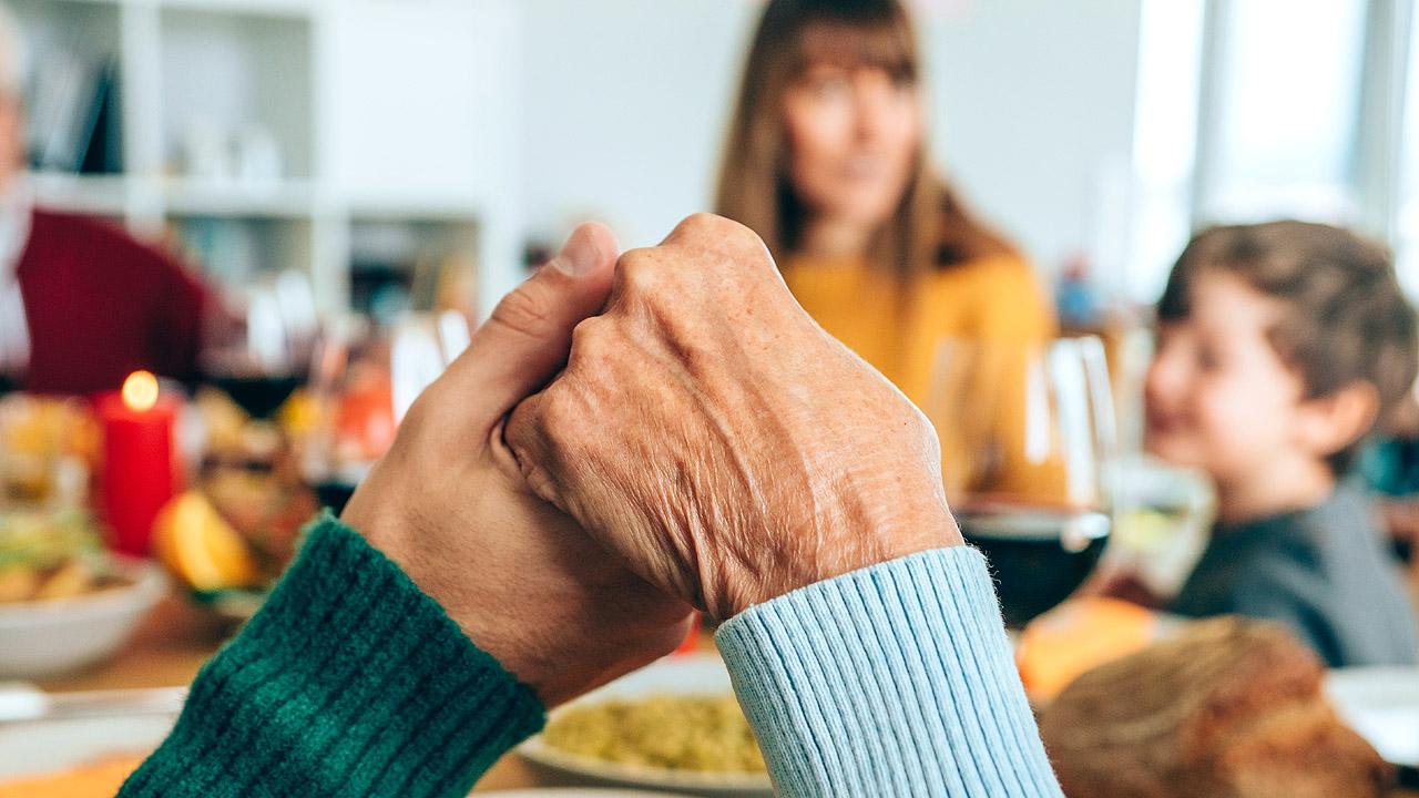 Menschen siten am Tisch und halten sich an den Händen, ihre Augen sind geschlossen