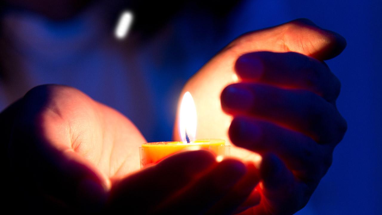 Eine Kerze wird in einer Hand gehalten, die andere schützt die Flamme vor Wind