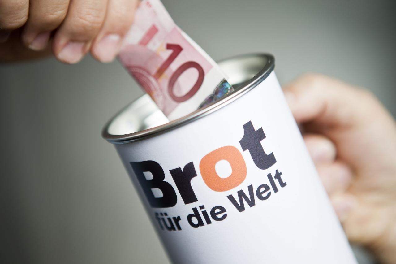 Spendendose Brot für die Welt Jemand steckt einen Zehn-Euro-Schein in eine Spendendose, auf der "Brot für die Welt" steht.