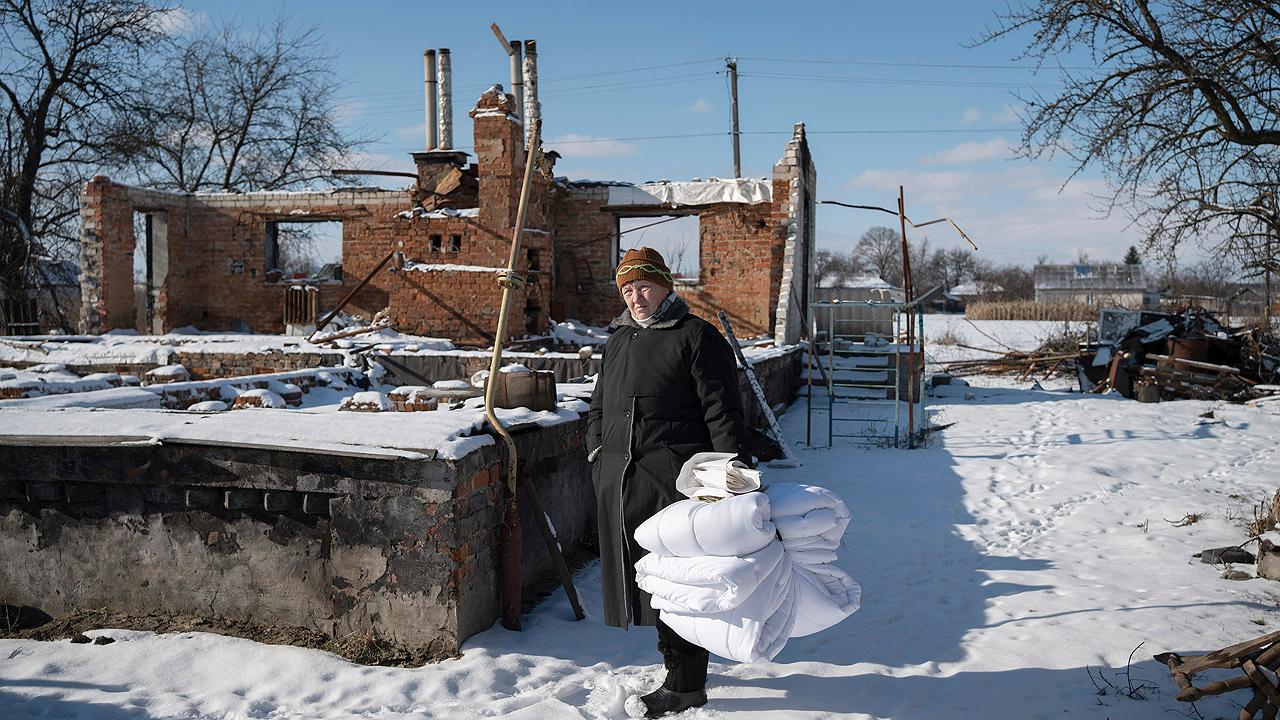 Frau mit Bettdecken vor einer Haus-Ruine