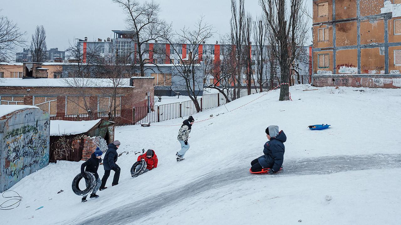 Winterhilfe Ukraine Kinder rodeln einen Hang herunter, dahinter Wohnblocks
