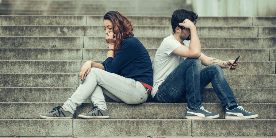 Ein jüngeres Paar, das sich gerade nicht viel zu erzählen hat Eine Frau und ein Mann sitzen gelangweilt Rücken an Rücken auf einer Treppe