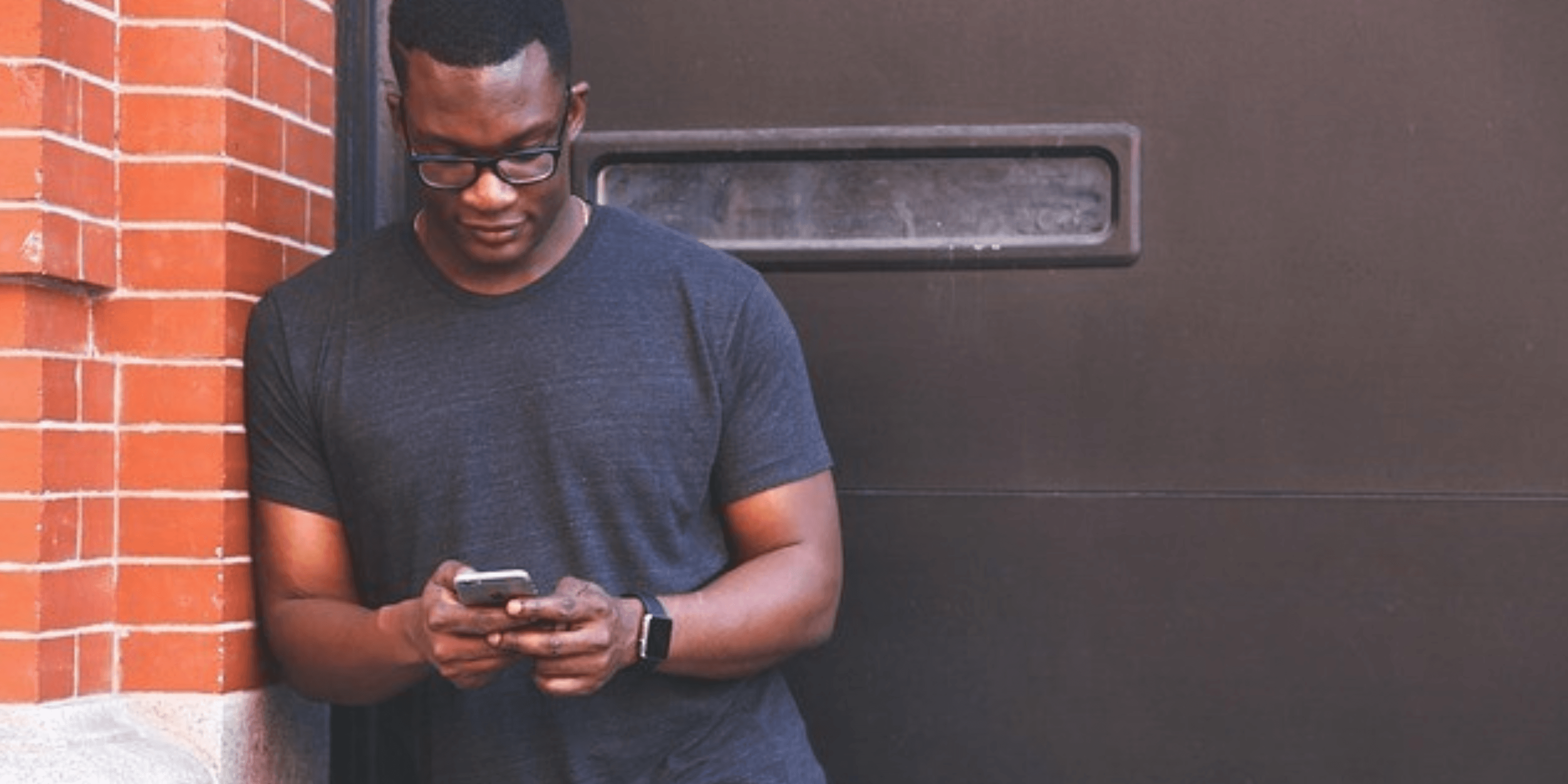 Mann vertreibt sich die Zeit am Handy schwarzer Mann steht vor einem Tor und schaut auf sein Handy