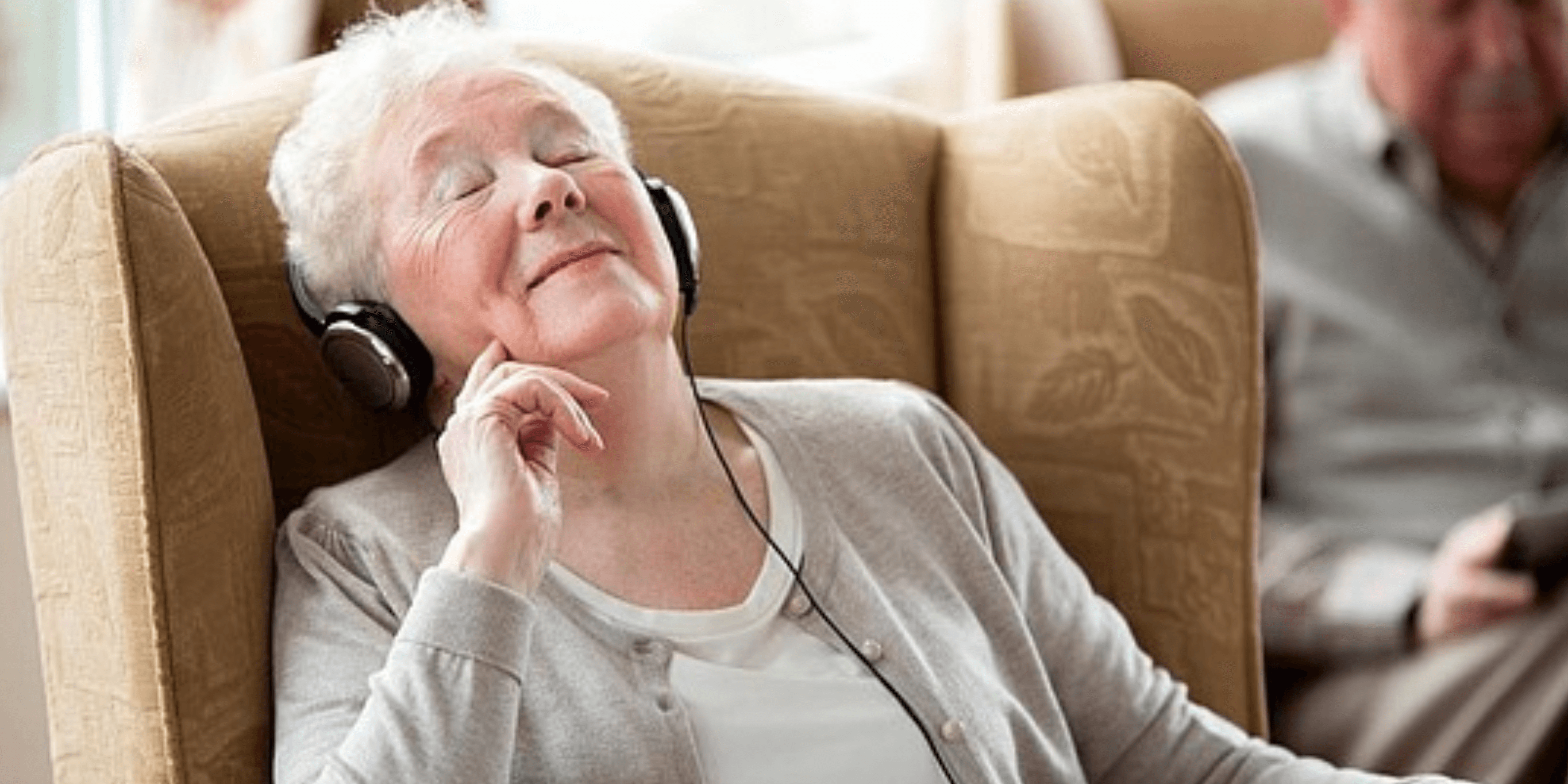 Eine Seniorin sitzt sichtlich genießend mit Kopfhörer im Sessel