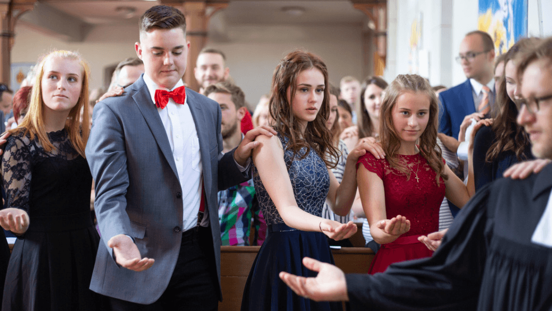 Im Konfirmationsgottesdienst Mehrere Konfirmand*innen im Gottesdienst umringen den Pfarrer