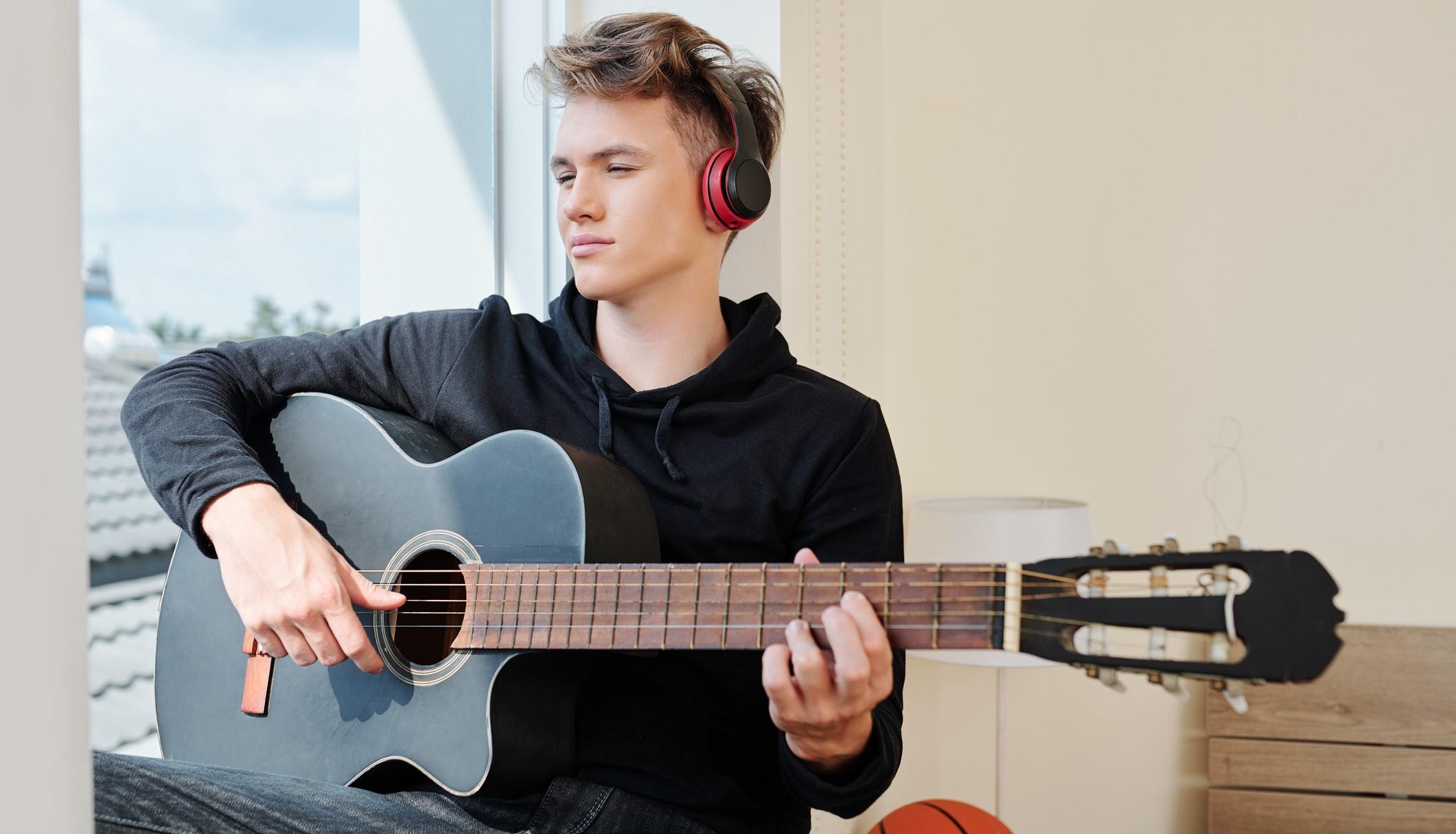 Gitarrenspieler Eine Junge, der Gitarre spielt und dabei Kopfhörer aufhat