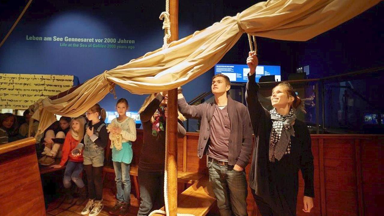 Boot im Bibelmuseum Eine Gruppe Jugendlicher steht um den Mast des Holzbootes